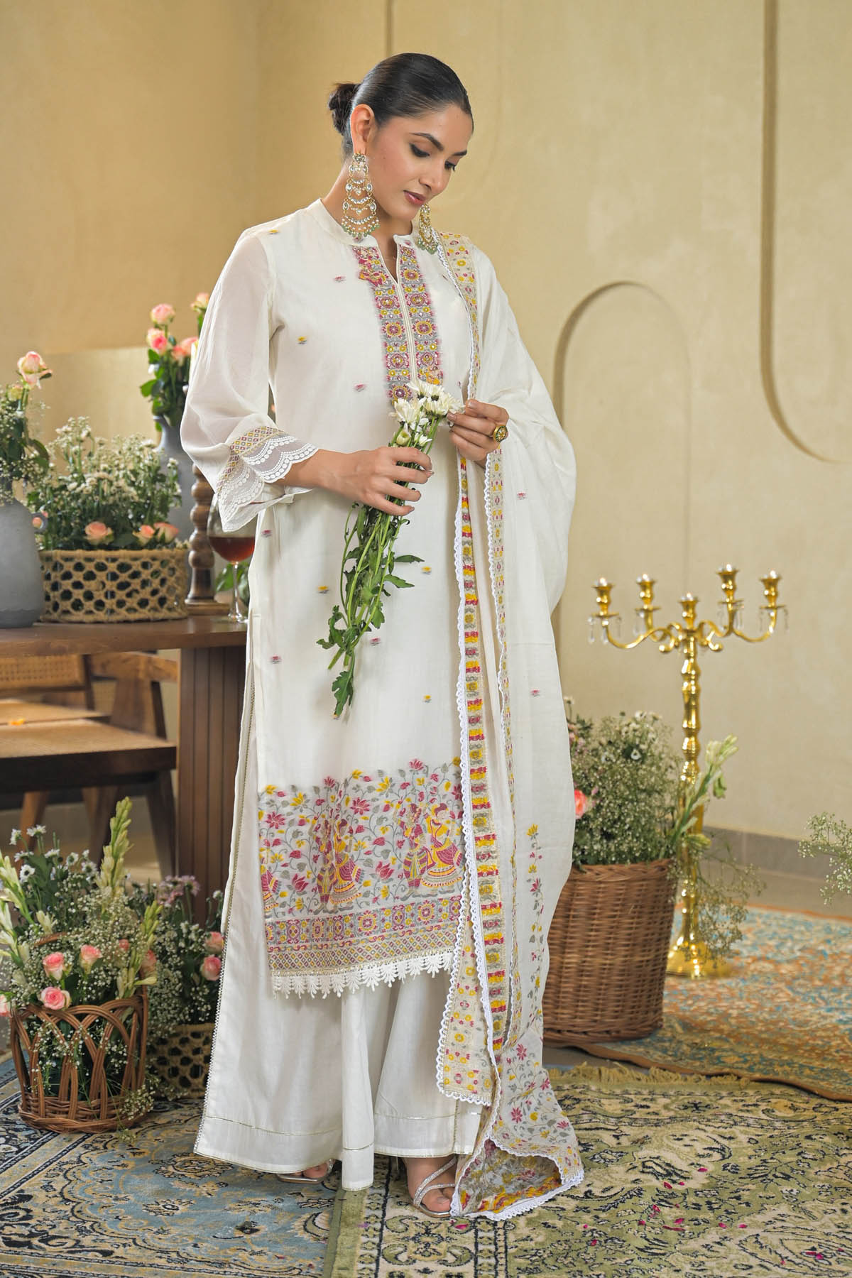 Woman in a white traditional outfit with floral patterns in an elegant indoor setting.