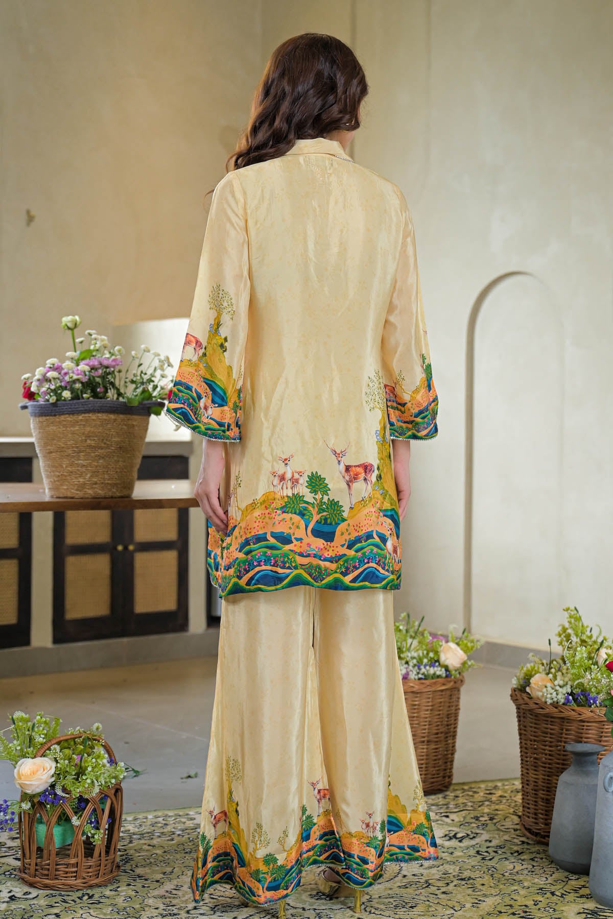 Woman wearing a cream-colored embroidered outfit in an indoor setting with decorative plants.
