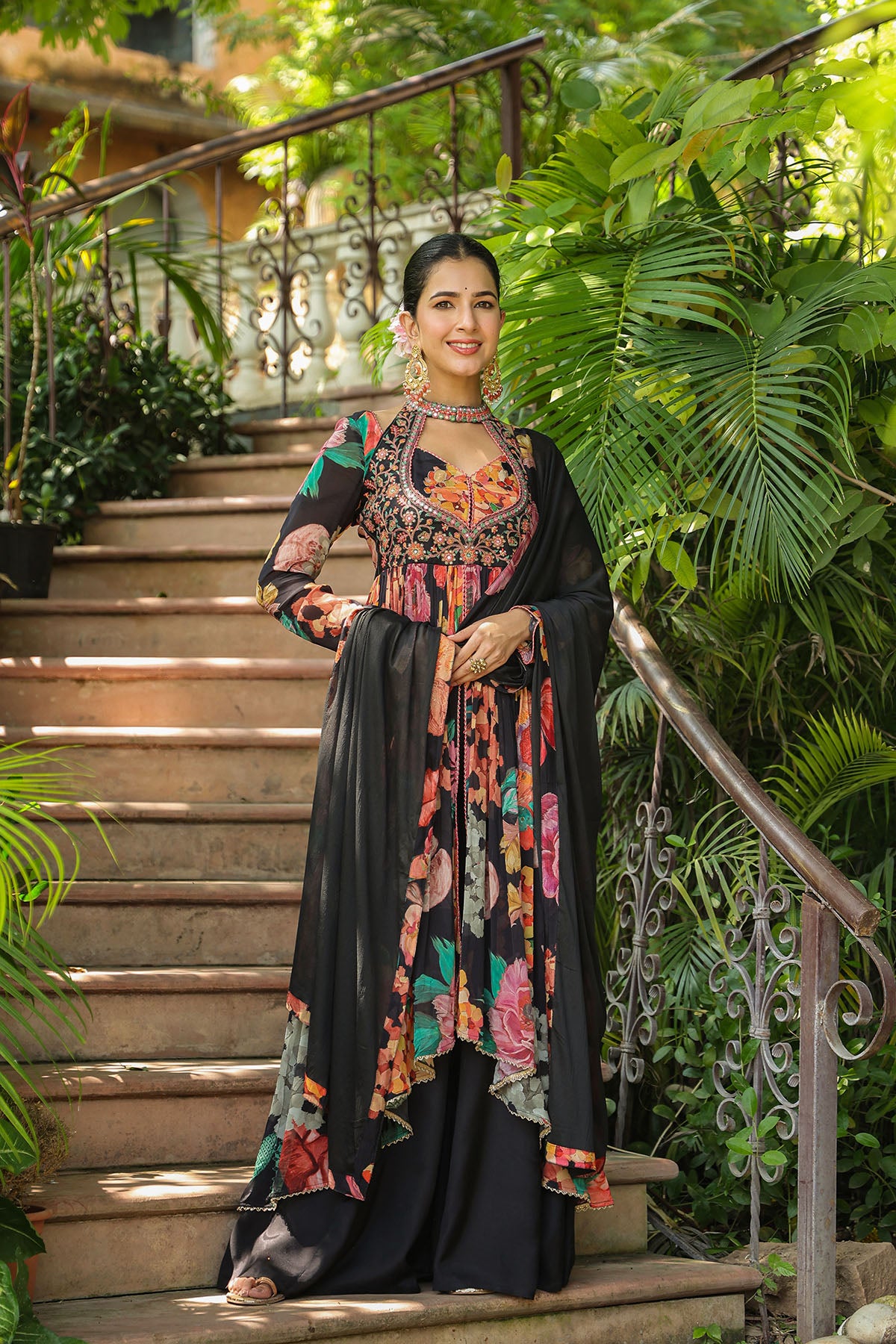 Woman in traditional outfit standing on a staircase surrounded by greenery