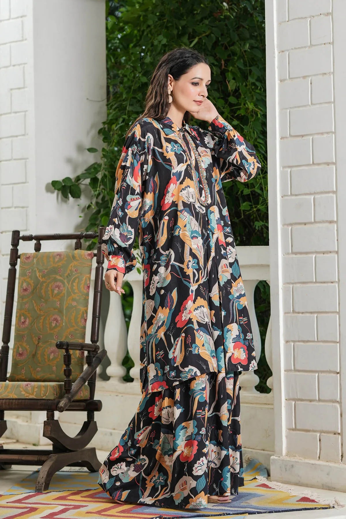 Woman in a colorful patterned dress standing in a doorway with a chair and rug in the foreground.