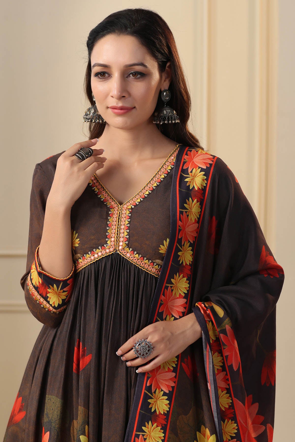 Woman wearing a dark brown dress with floral patterns and jewelry indoors.