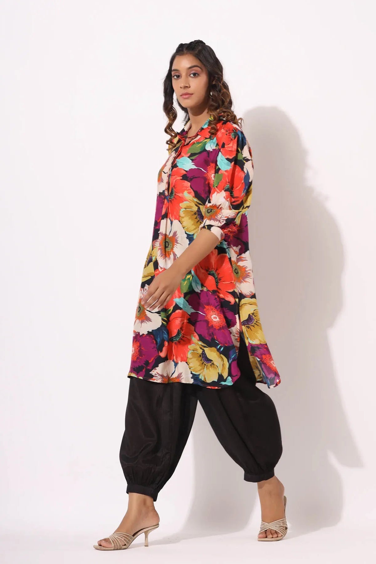 Woman wearing a colorful floral dress with black pants on a white background