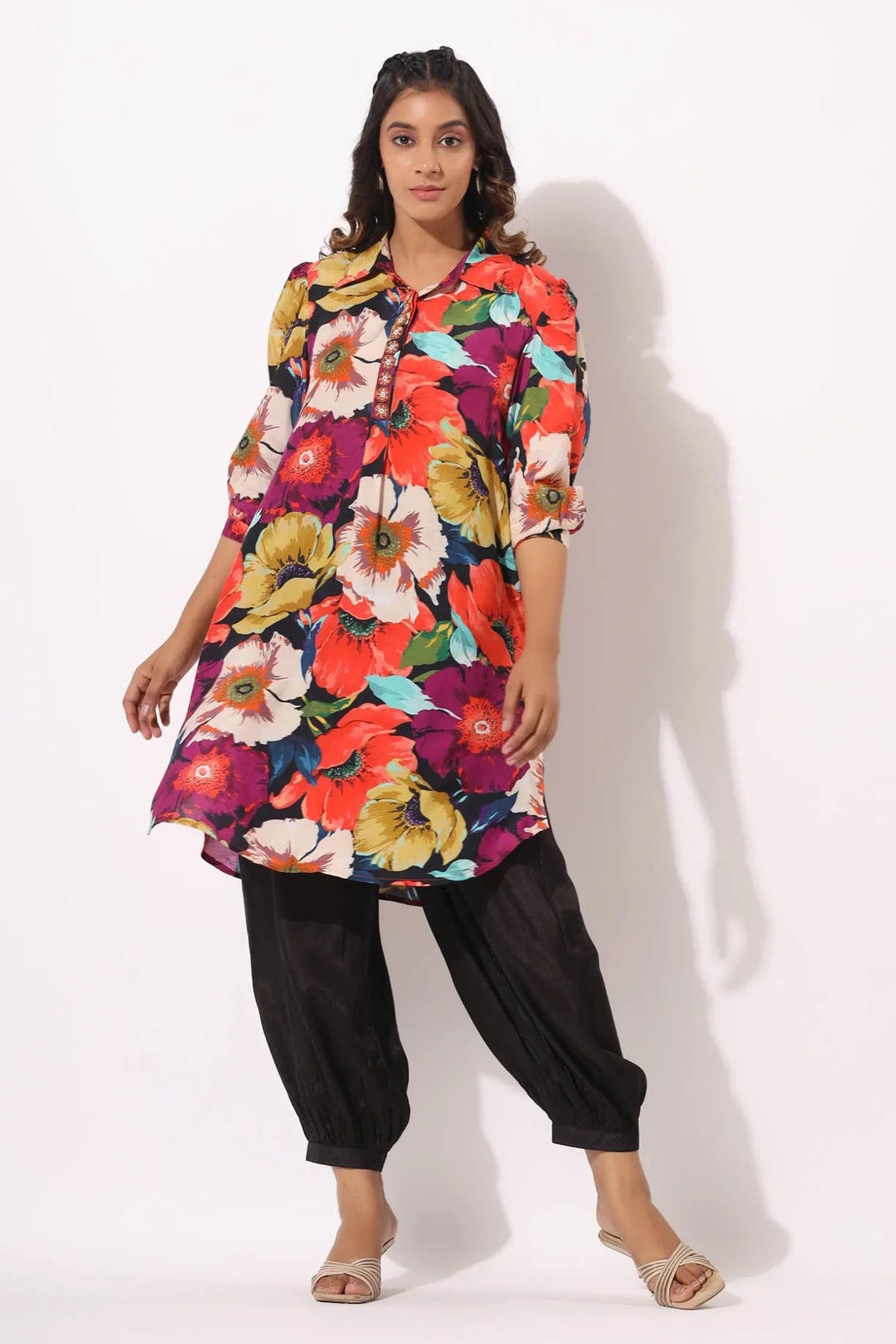 Woman wearing a colorful floral dress with black pants on a white background