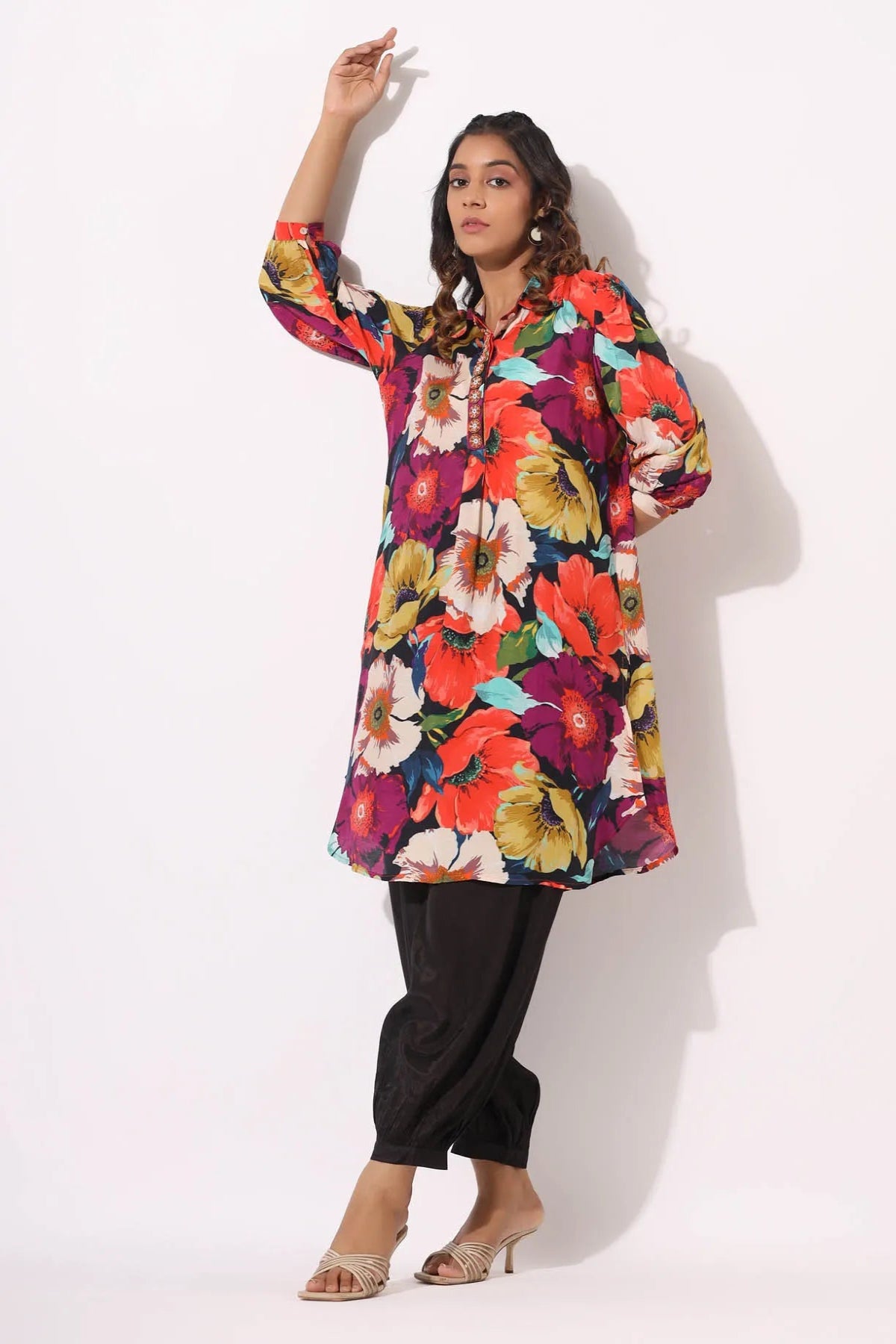 Woman wearing a colorful floral dress with black pants on a white background