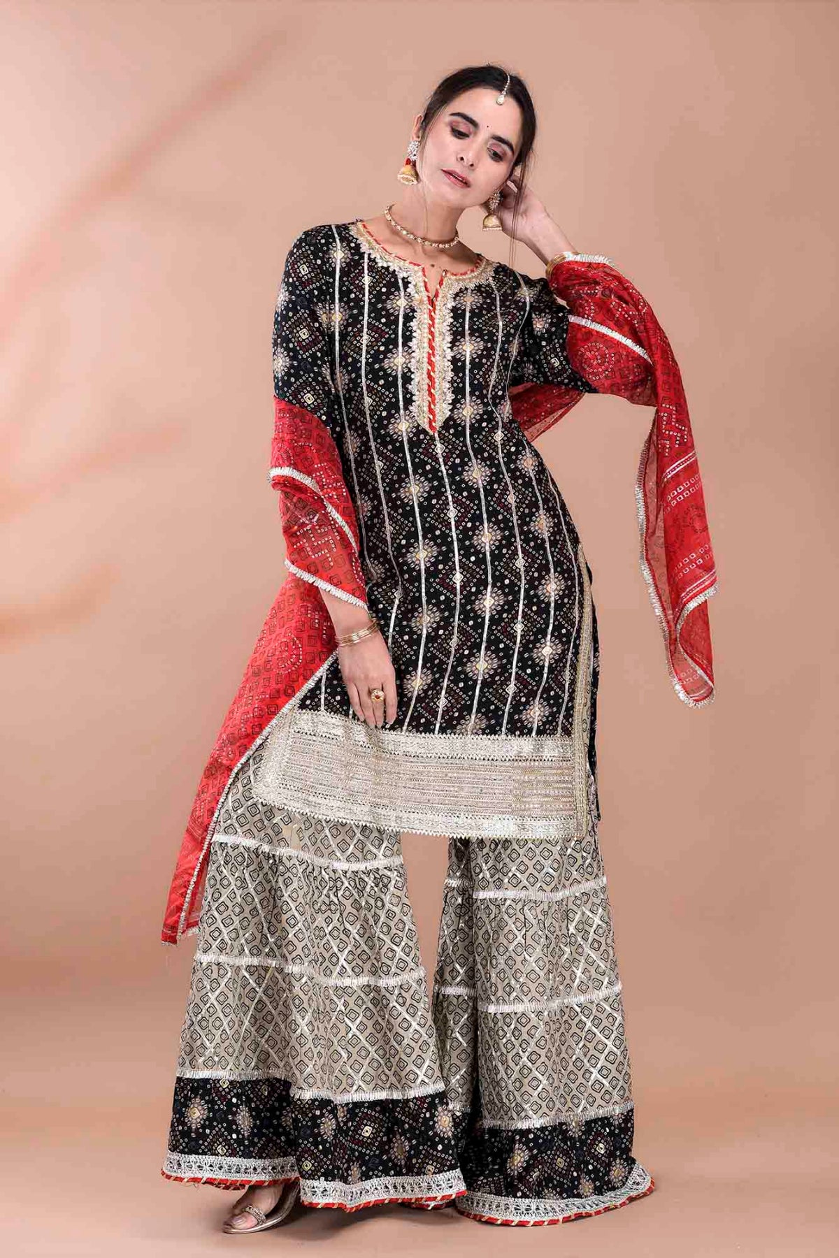 Woman wearing a black and white traditional outfit with a red dupatta on a beige background