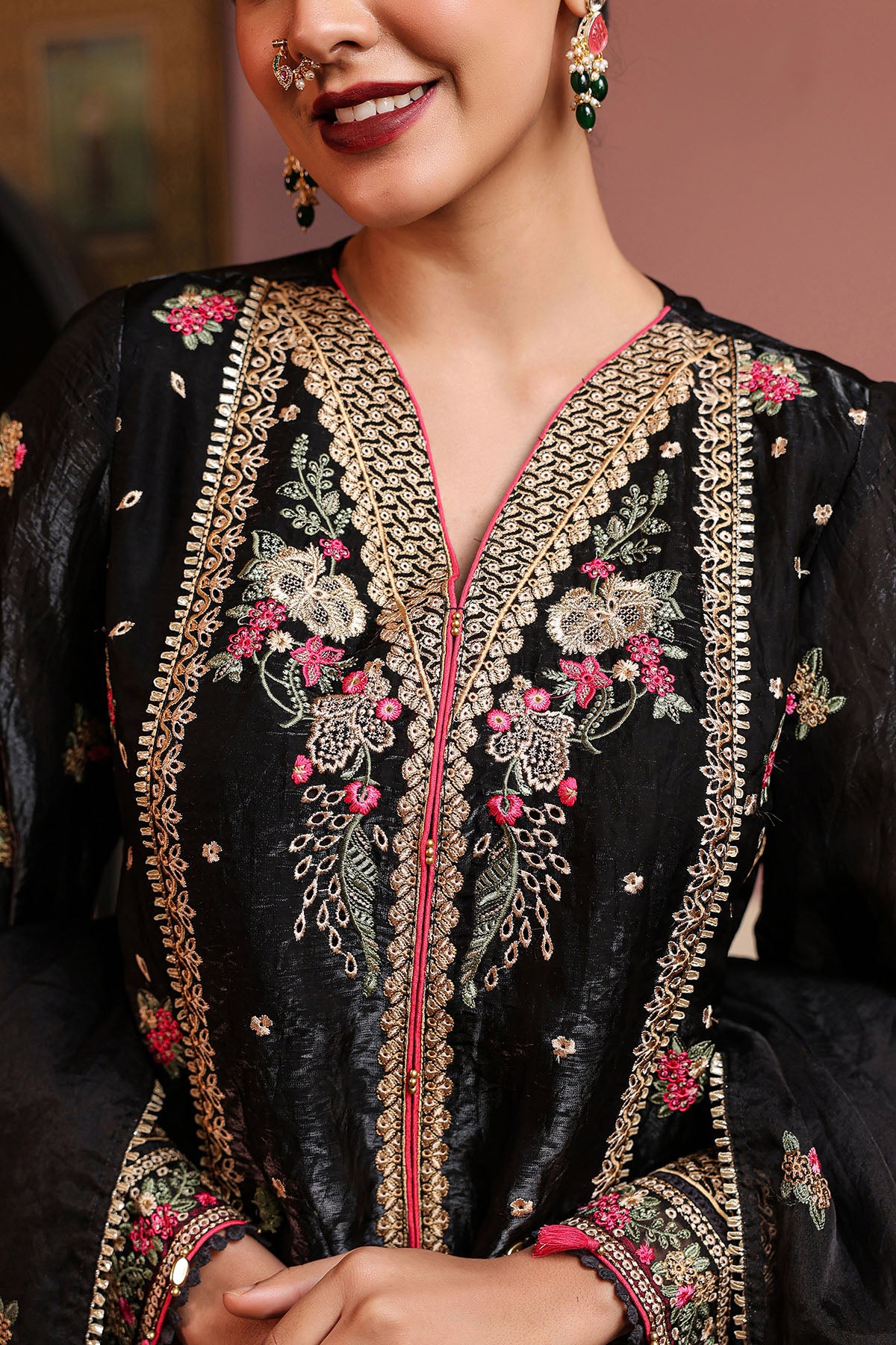 Woman wearing a black embroidered outfit with gold and pink details.