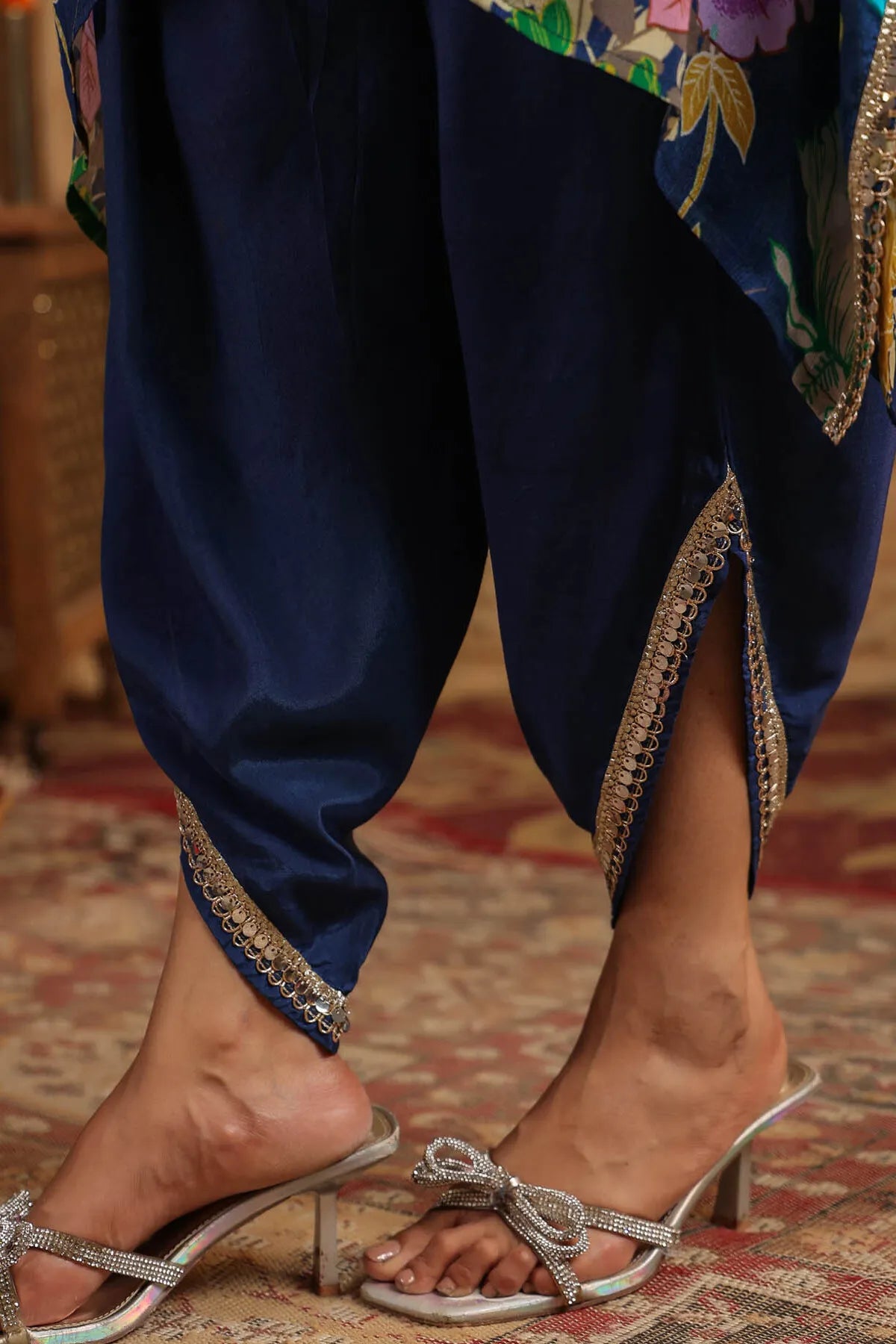 Navy blue traditional outfit with floral patterns and silver sandals on a patterned rug.