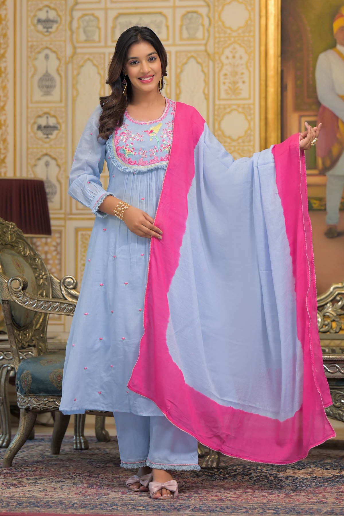 Woman in a light blue outfit with pink dupatta in an ornate room