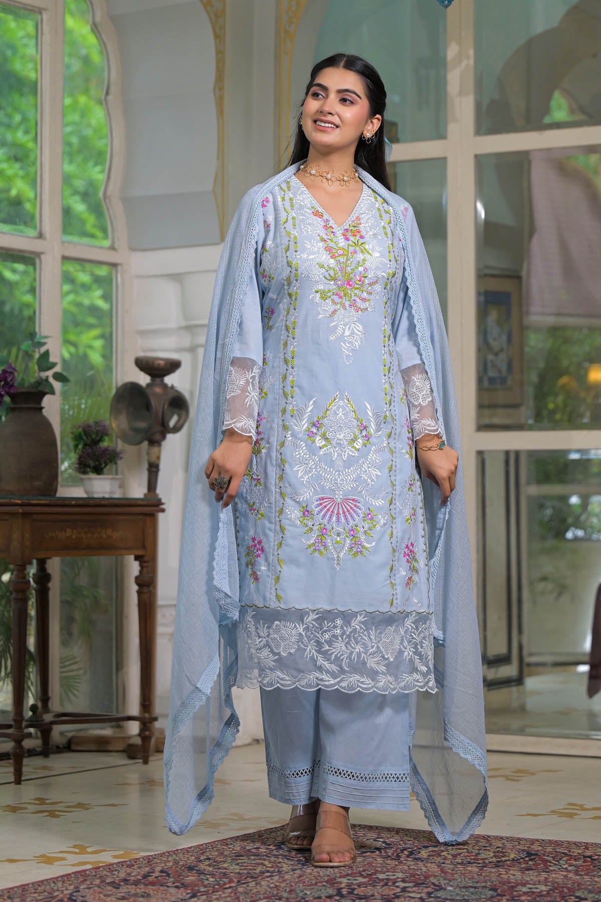 Woman wearing a light blue embroidered traditional outfit in an indoor setting.