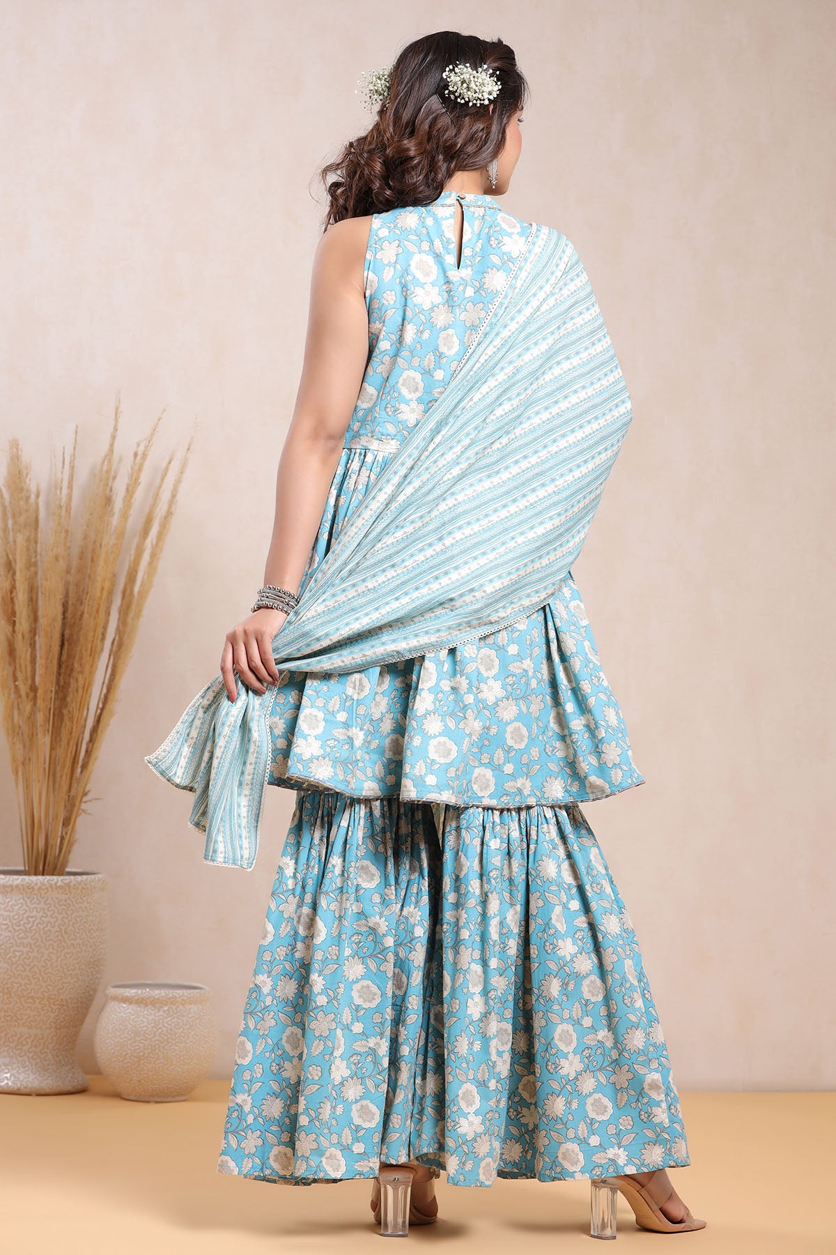 Woman wearing a light blue floral saree with a matching blouse against a beige background
