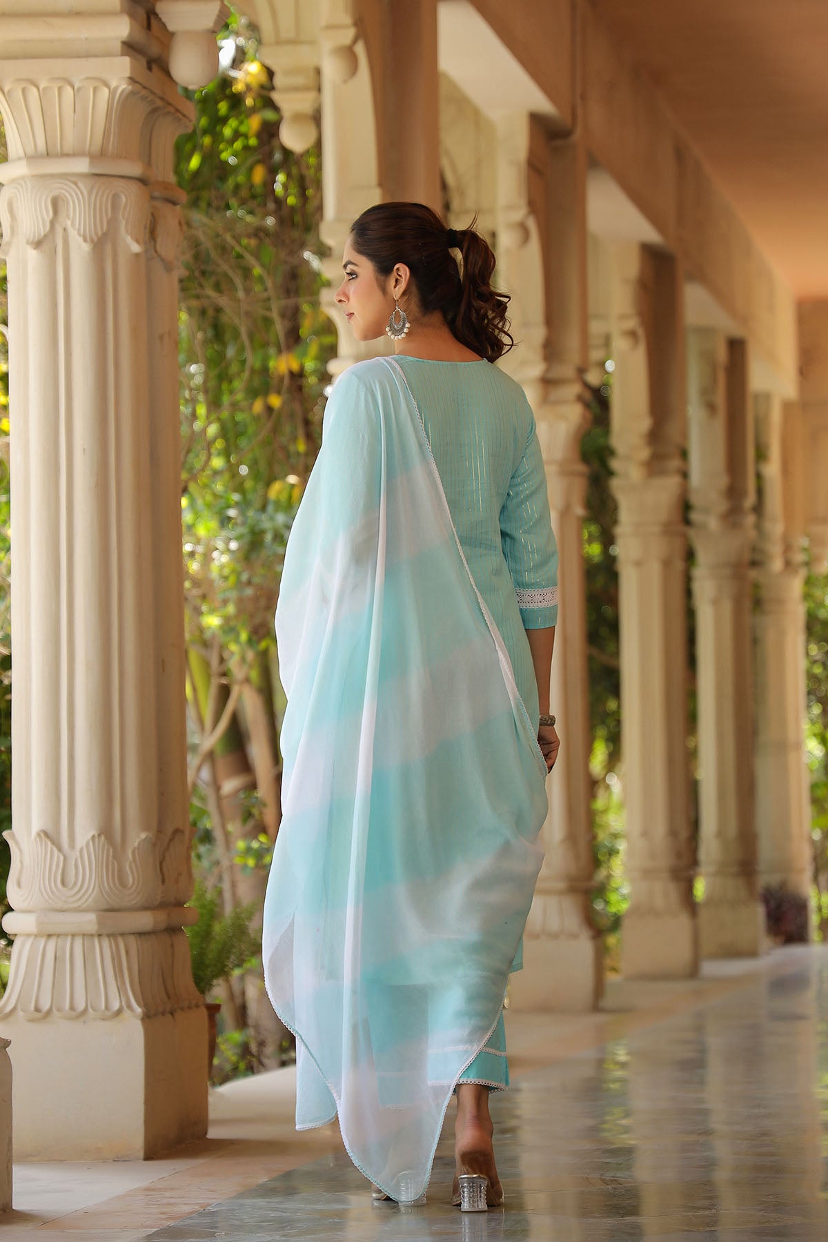 Woman in a light blue saree walking along a corridor with columns.