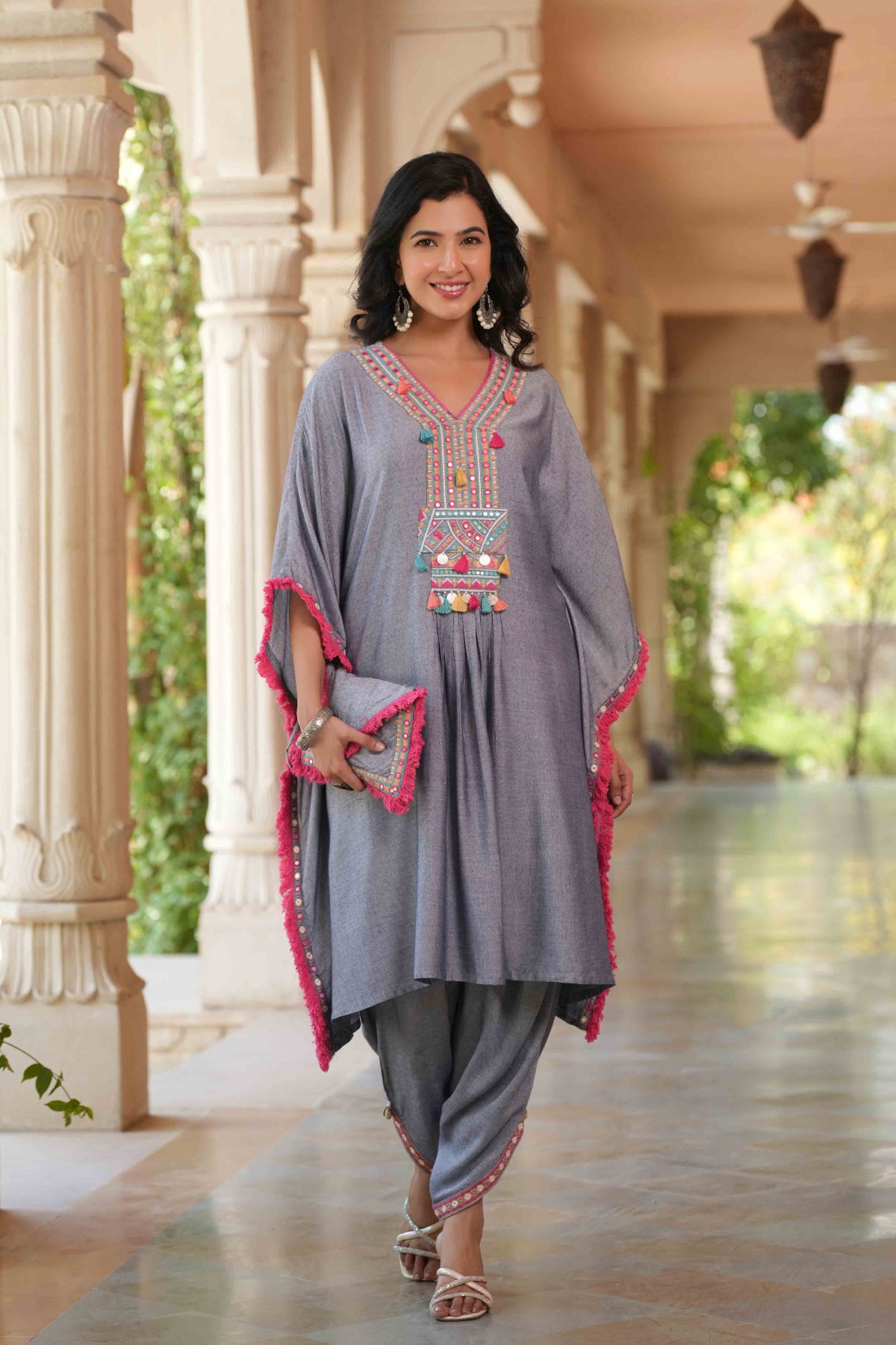 Woman in traditional outfit with embroidered top and dhoti standing in a decorative outdoor setting.