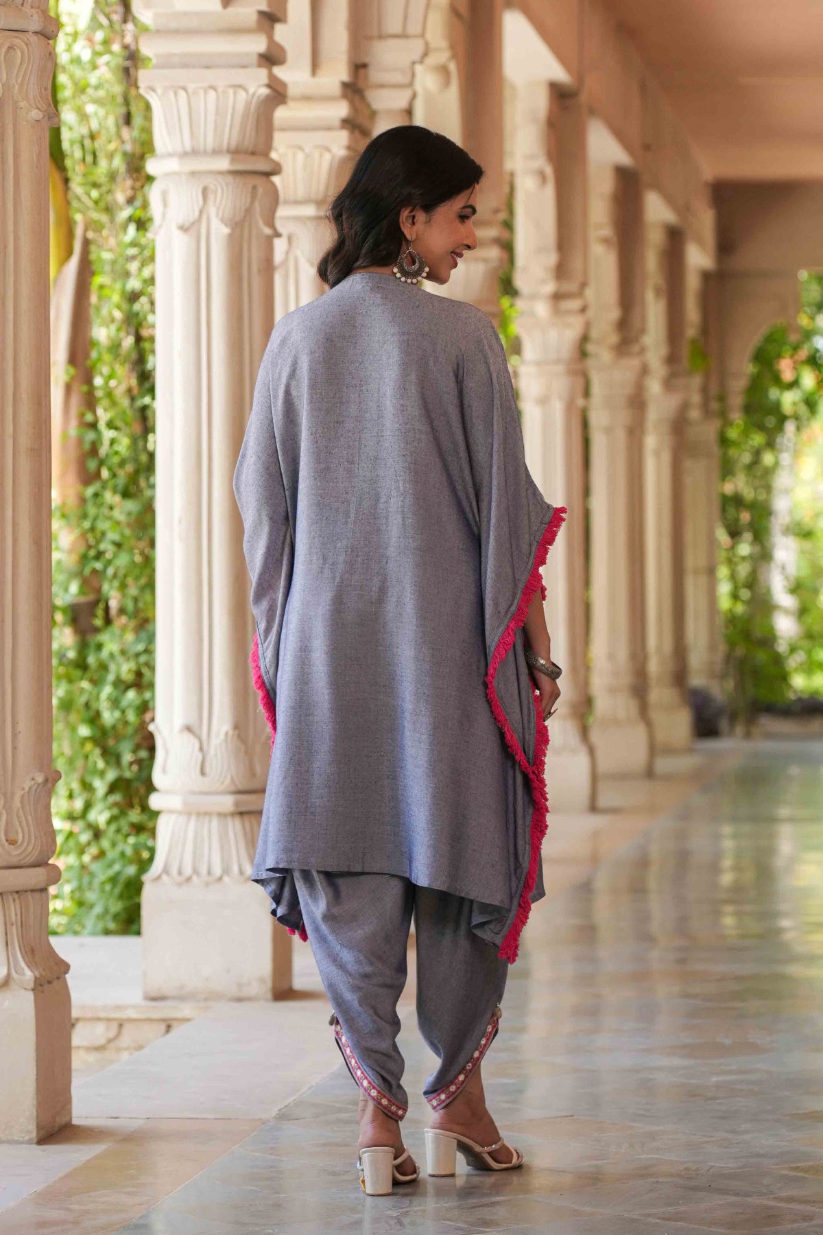 Woman in a gray traditional outfit with red accents standing in a decorative corridor.