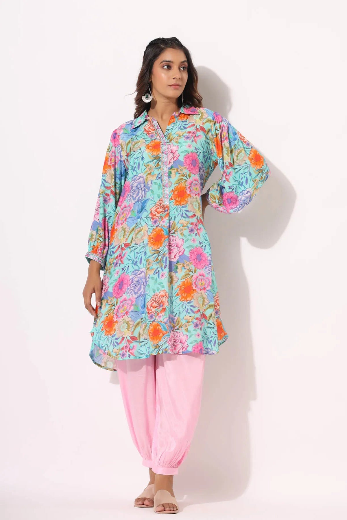 Woman wearing a colorful floral top and pink pants on a white background