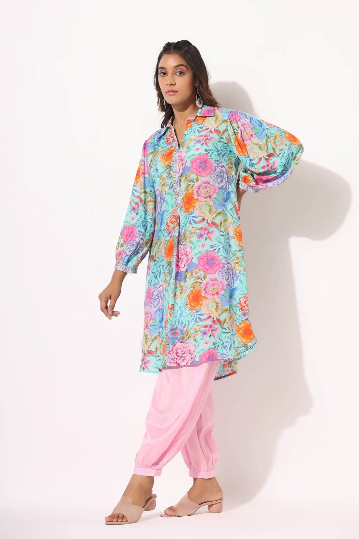 Woman wearing a colorful floral top and pink pants on a white background