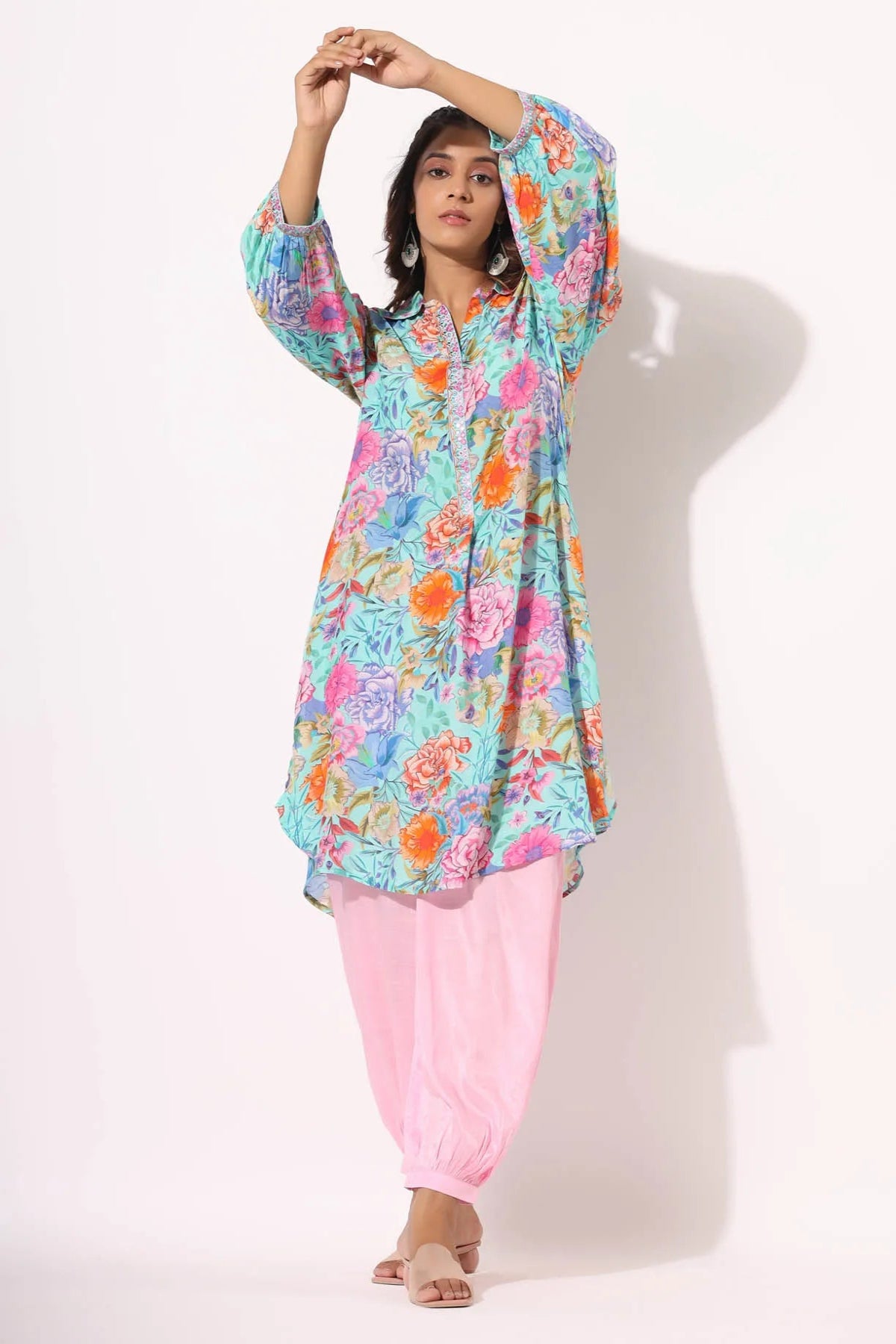 Woman wearing a colorful floral top and pink pants on a white background
