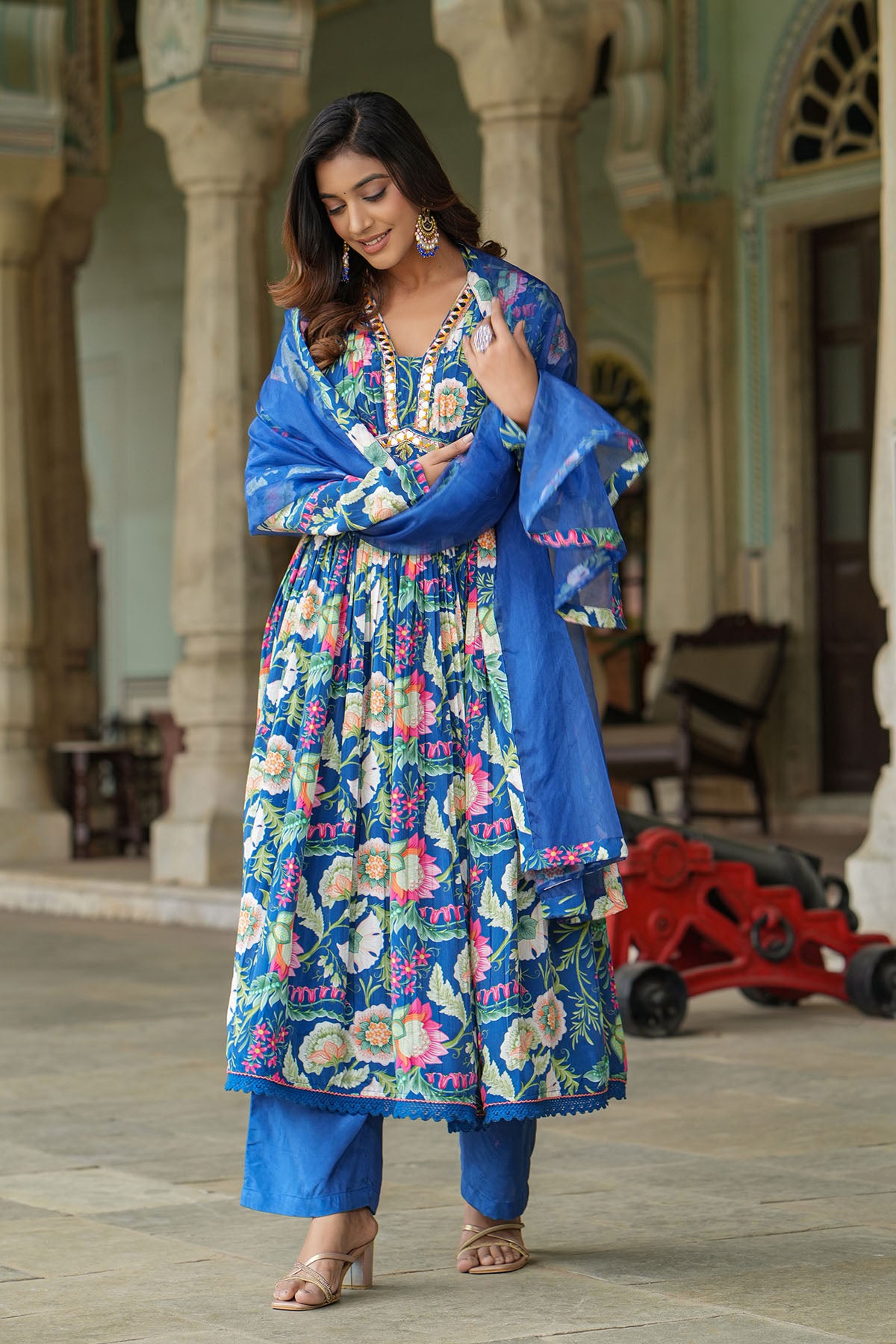 Woman in a colorful traditional outfit with a blue dupatta standing in an outdoor setting.