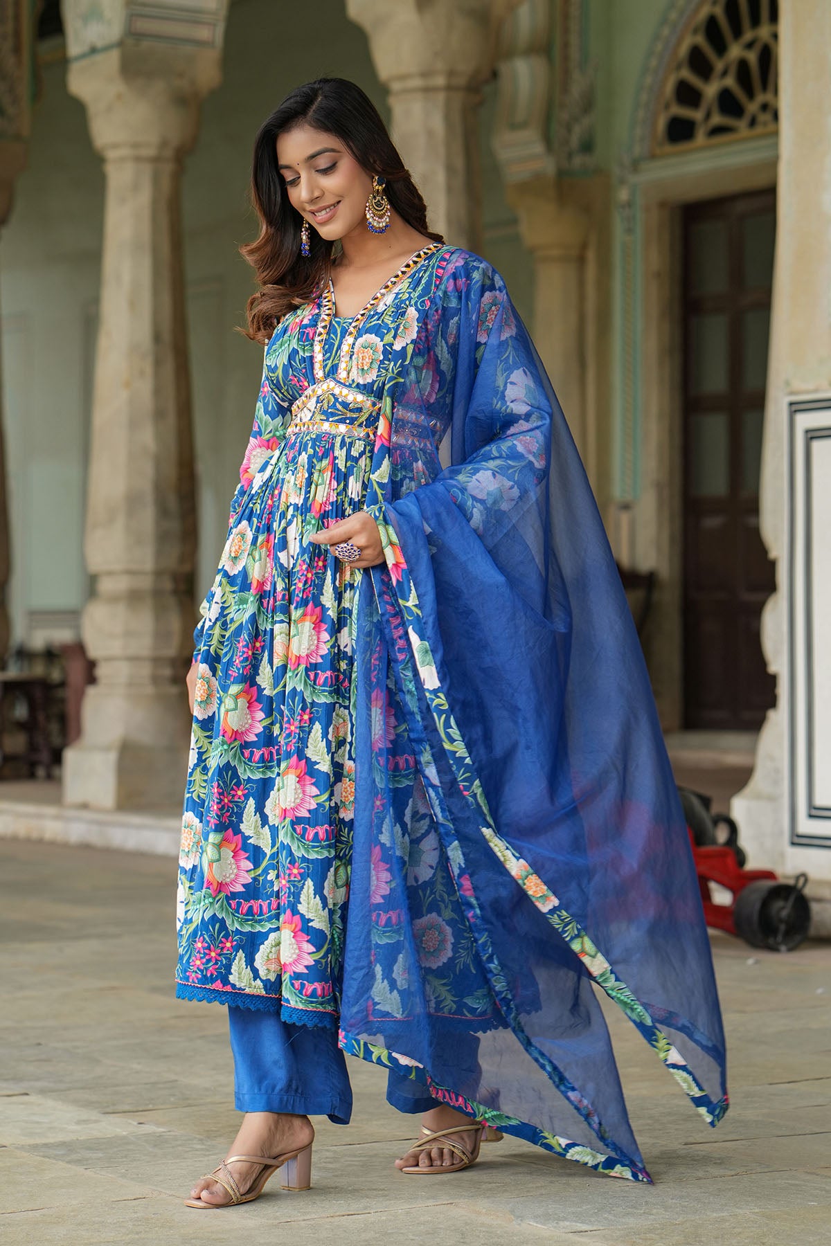 Woman in a colorful traditional outfit with a blue dupatta standing in an outdoor setting.