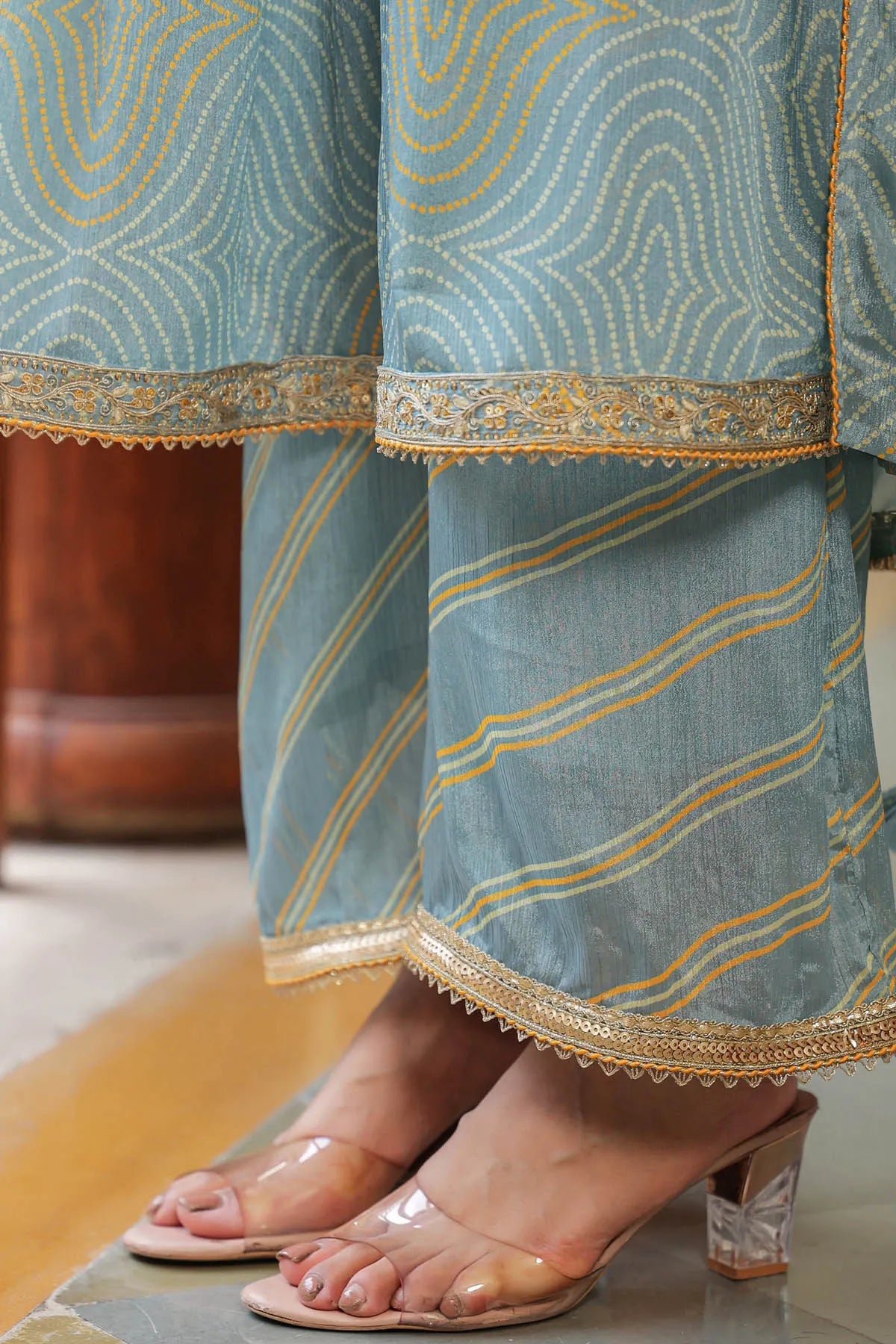 Close-up of a person wearing a blue traditional outfit with gold embroidery and transparent sandals.