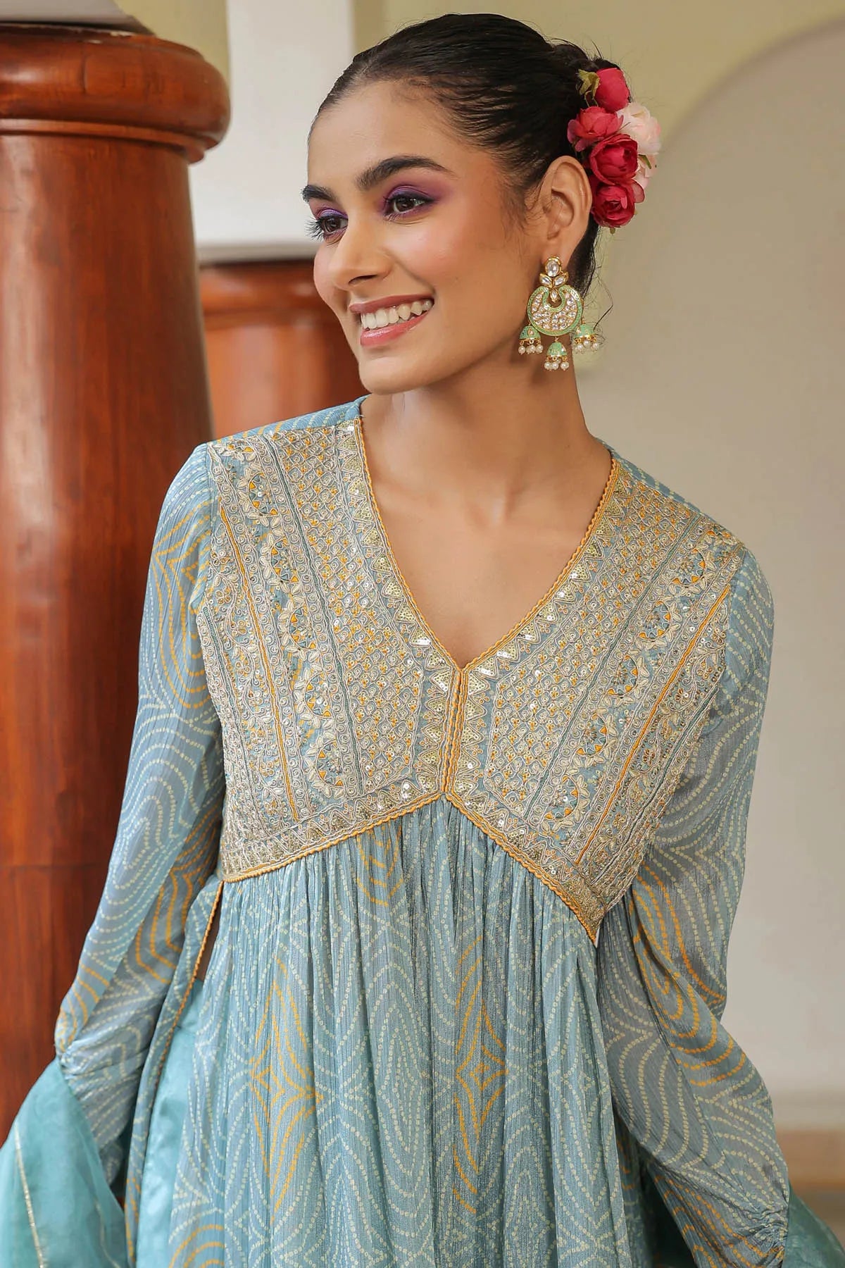 Woman wearing a light blue embroidered traditional outfit with gold details indoors.