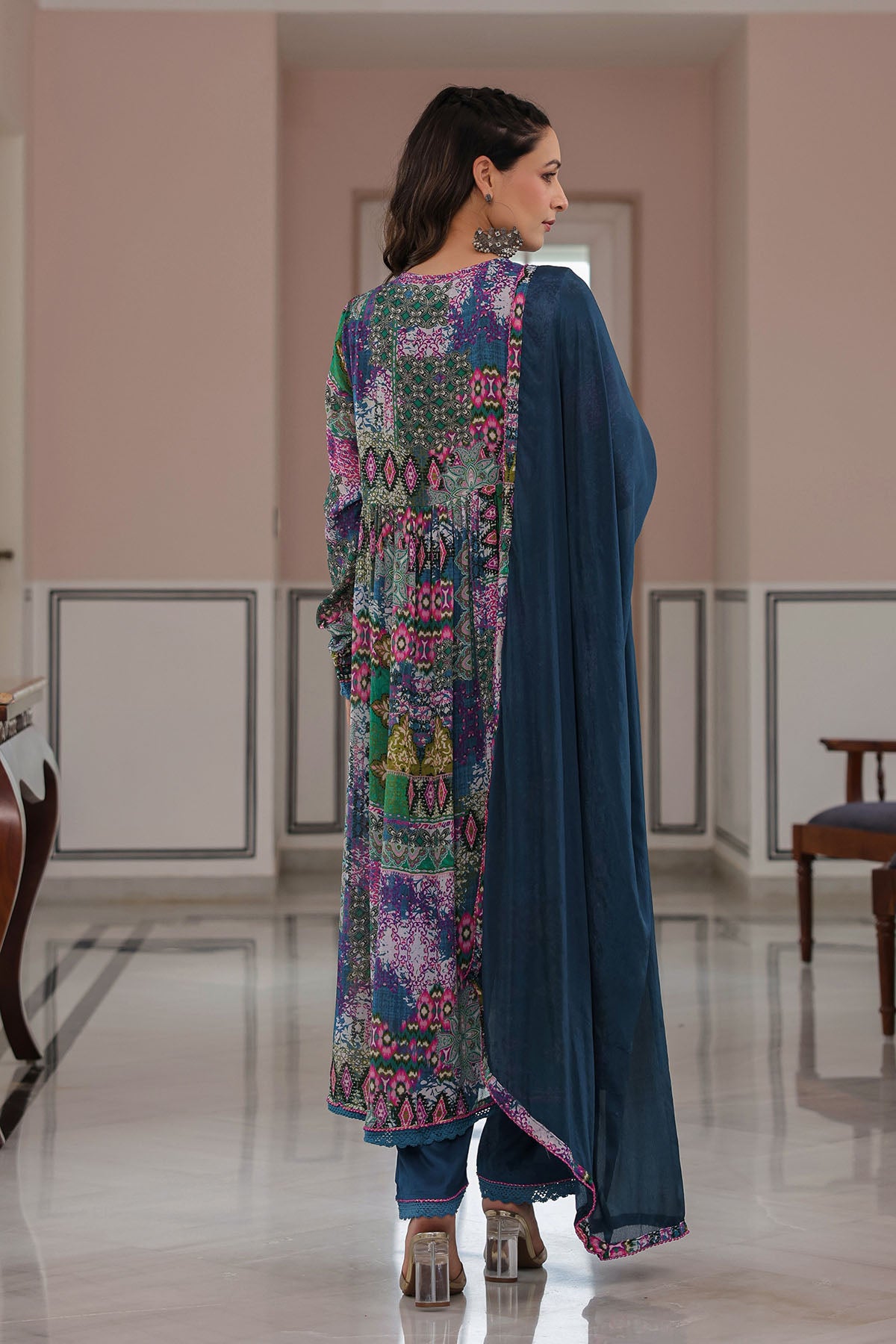 Woman wearing a colorful embroidered outfit with a blue dupatta in an indoor setting.