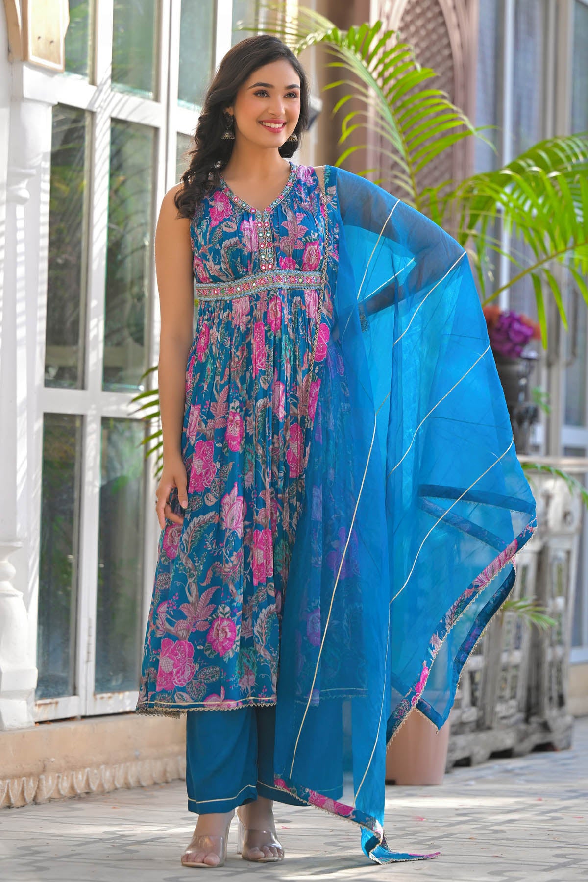 Woman in a floral dress with a blue dupatta standing outdoors.