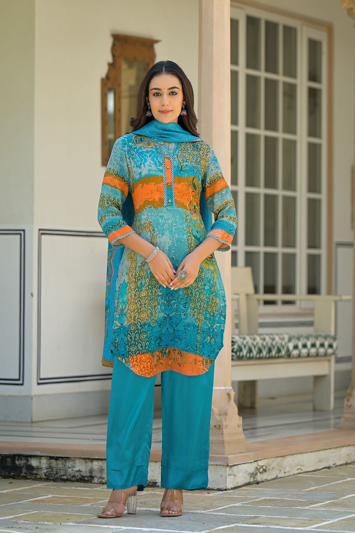 Woman wearing a blue and orange traditional outfit standing in front of a building.