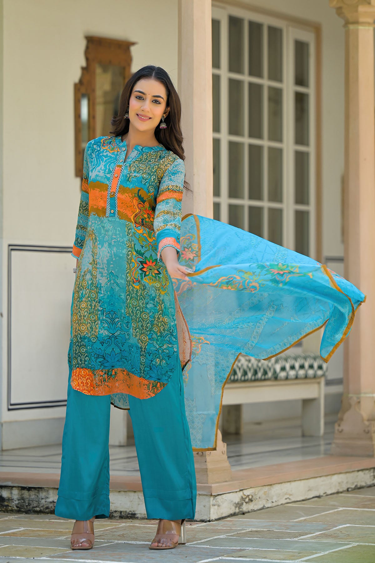 Woman in a teal and orange traditional outfit holding a matching dupatta outdoors.