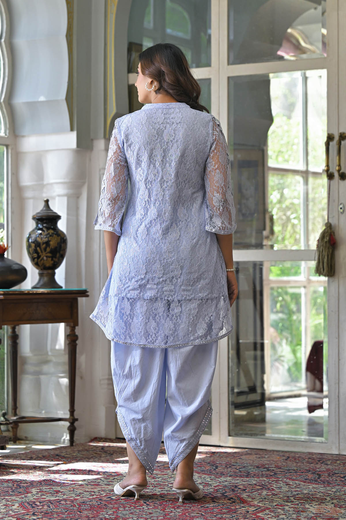 Woman in a light blue traditional outfit walking in a room with decorative elements.