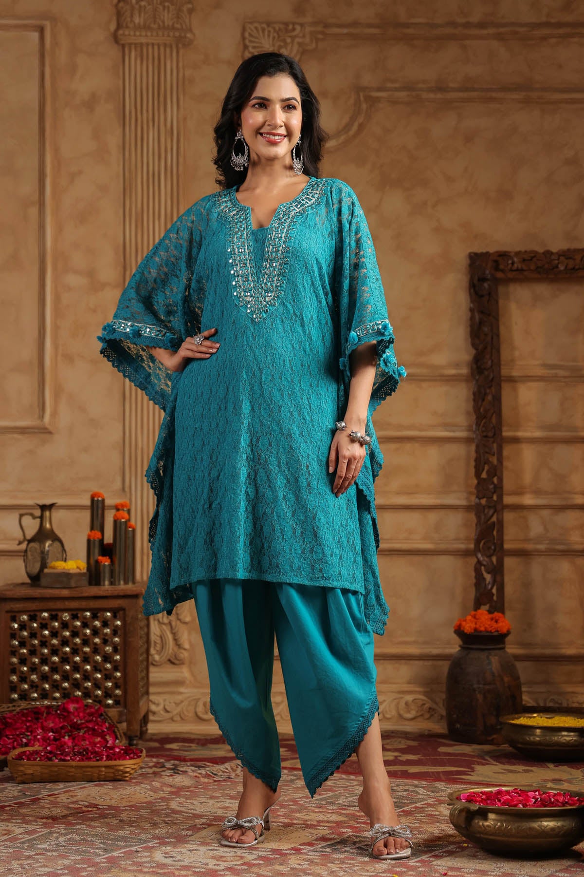 Woman in a teal traditional outfit standing in a decorated room.