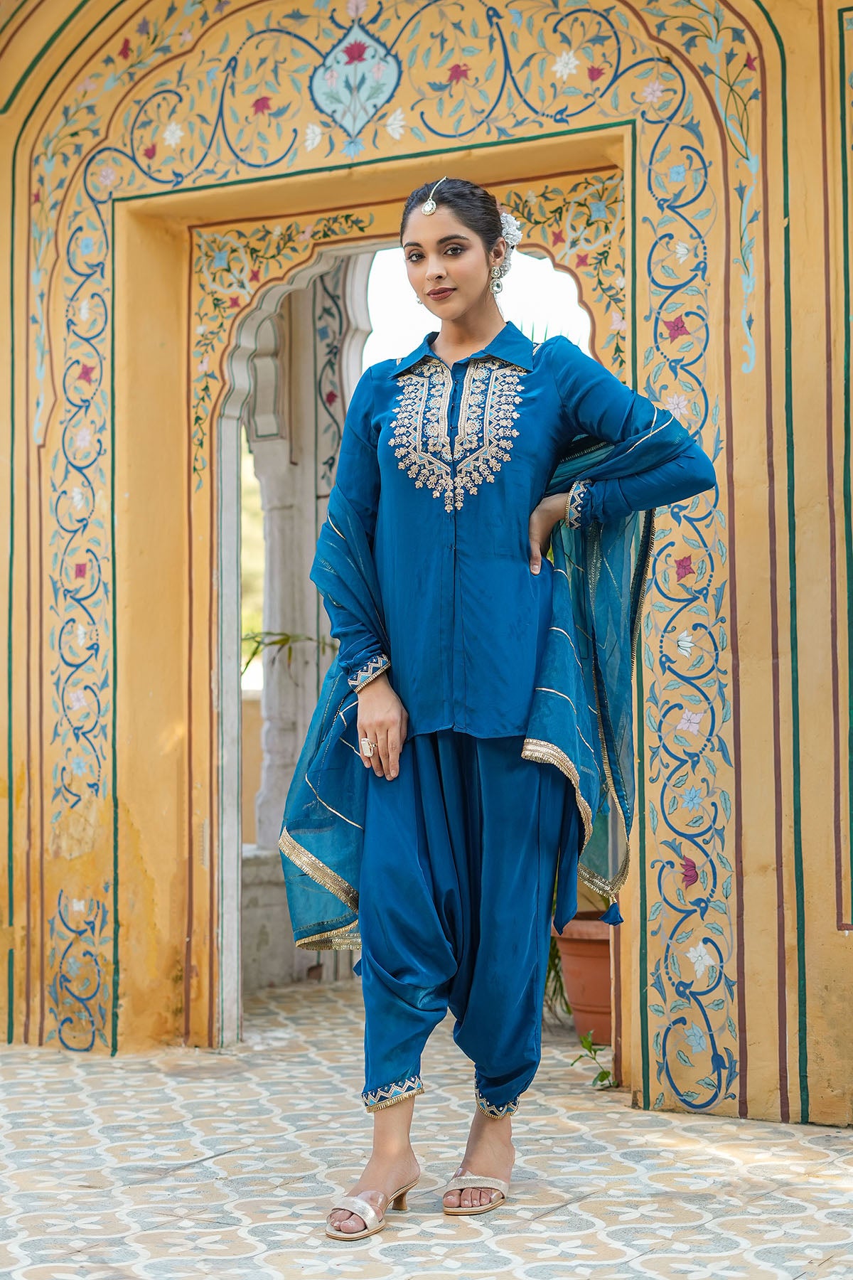 Woman in a blue traditional outfit standing in front of an ornate archway.
