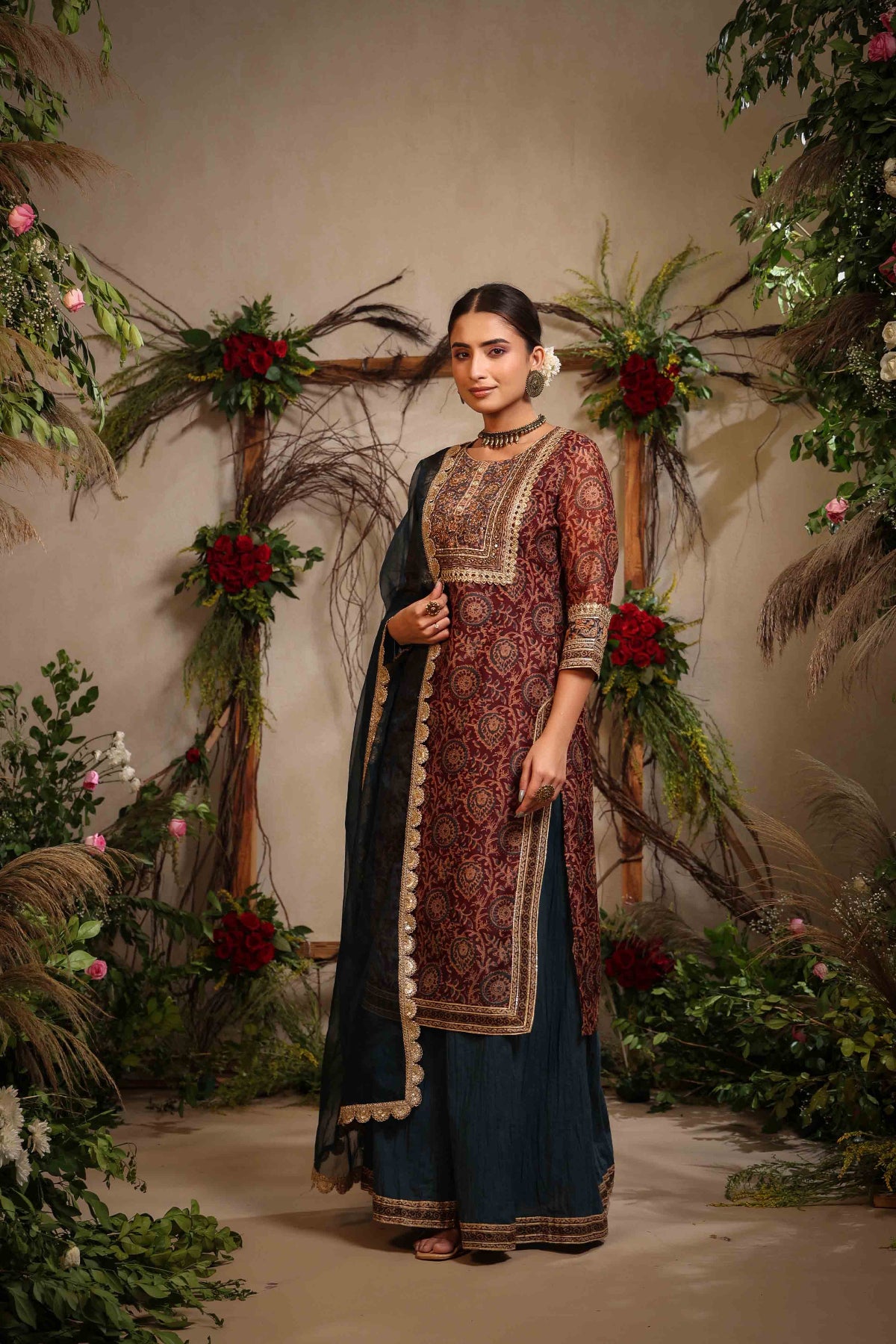 Woman in traditional outfit standing in a decorated indoor setting with floral arrangements.