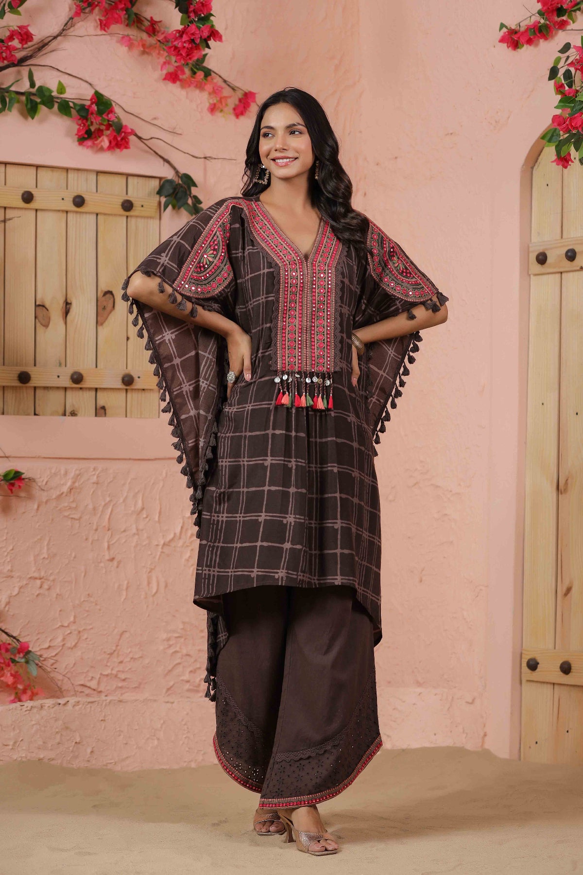 Woman wearing a traditional outfit with a checkered pattern in front of a pink wall with floral decorations.