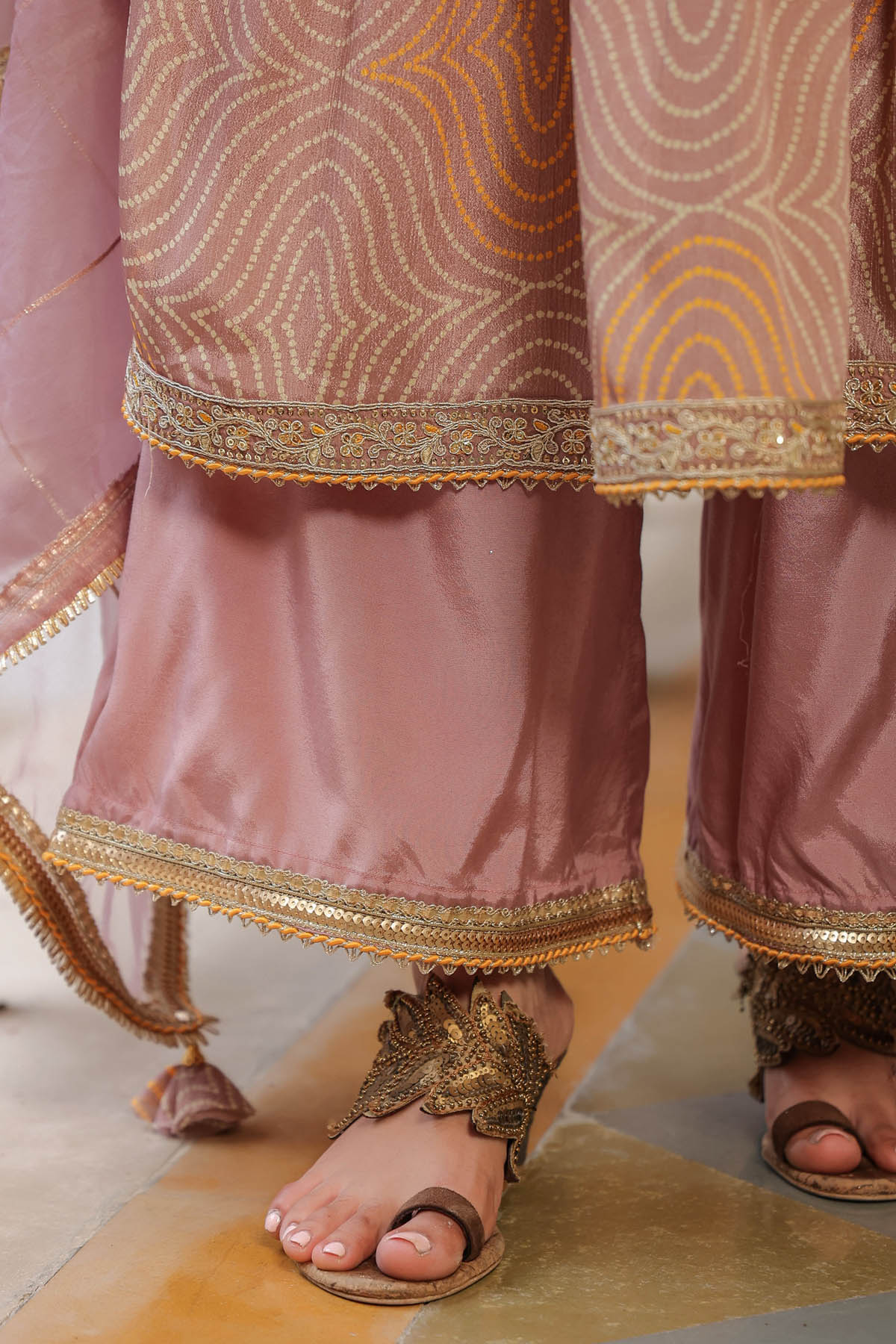 Close-up of a person wearing a traditional outfit with pink and gold embroidery on a light background.
