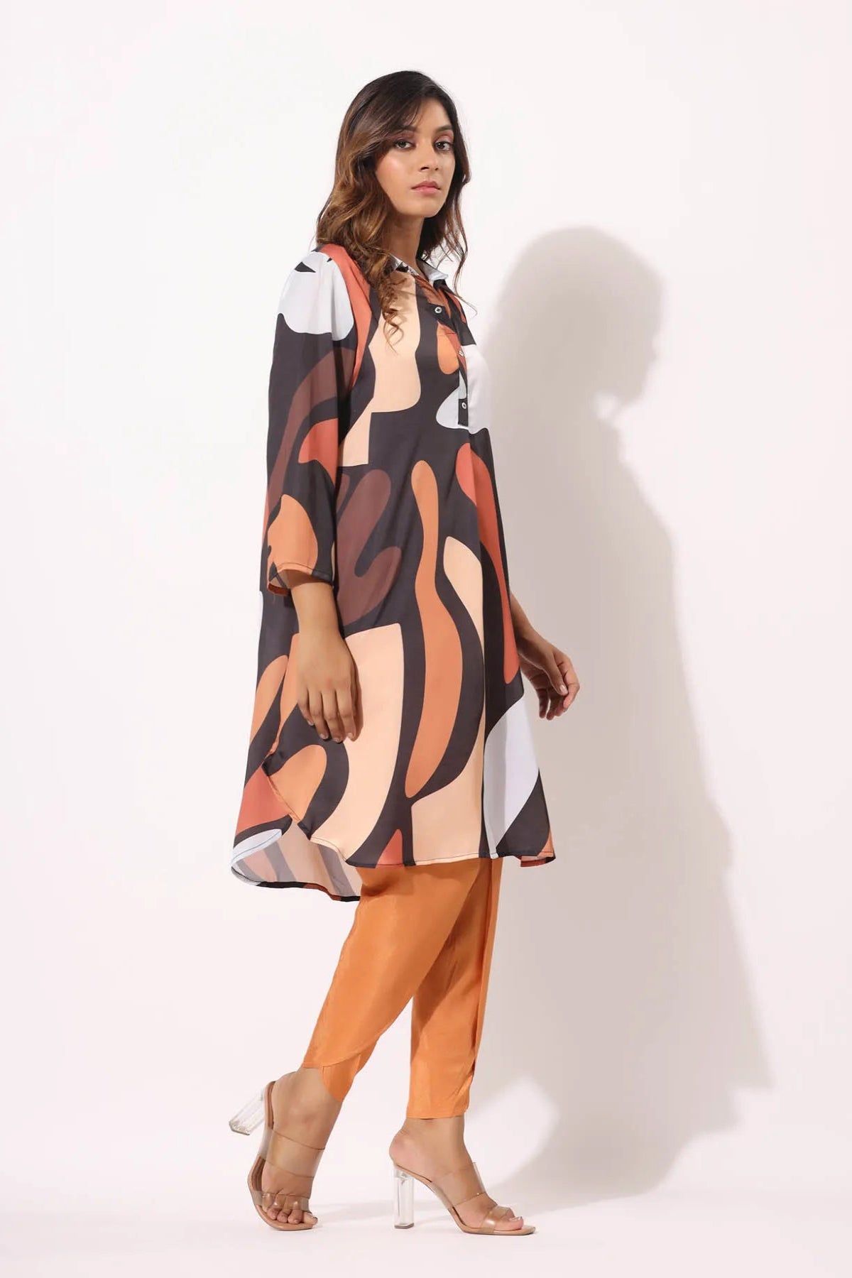 Woman wearing a patterned dress and orange pants on a white background