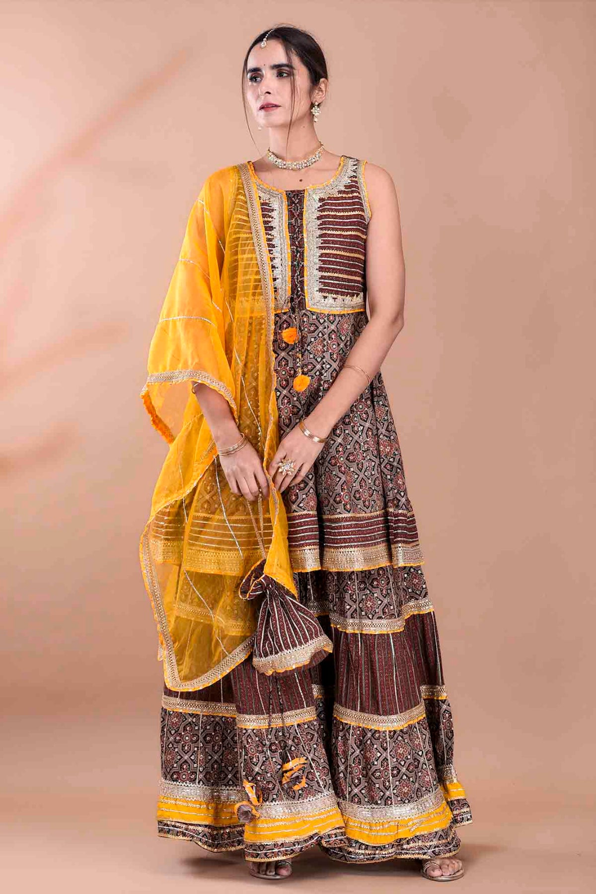 Woman wearing a traditional outfit with a yellow dupatta on a beige background