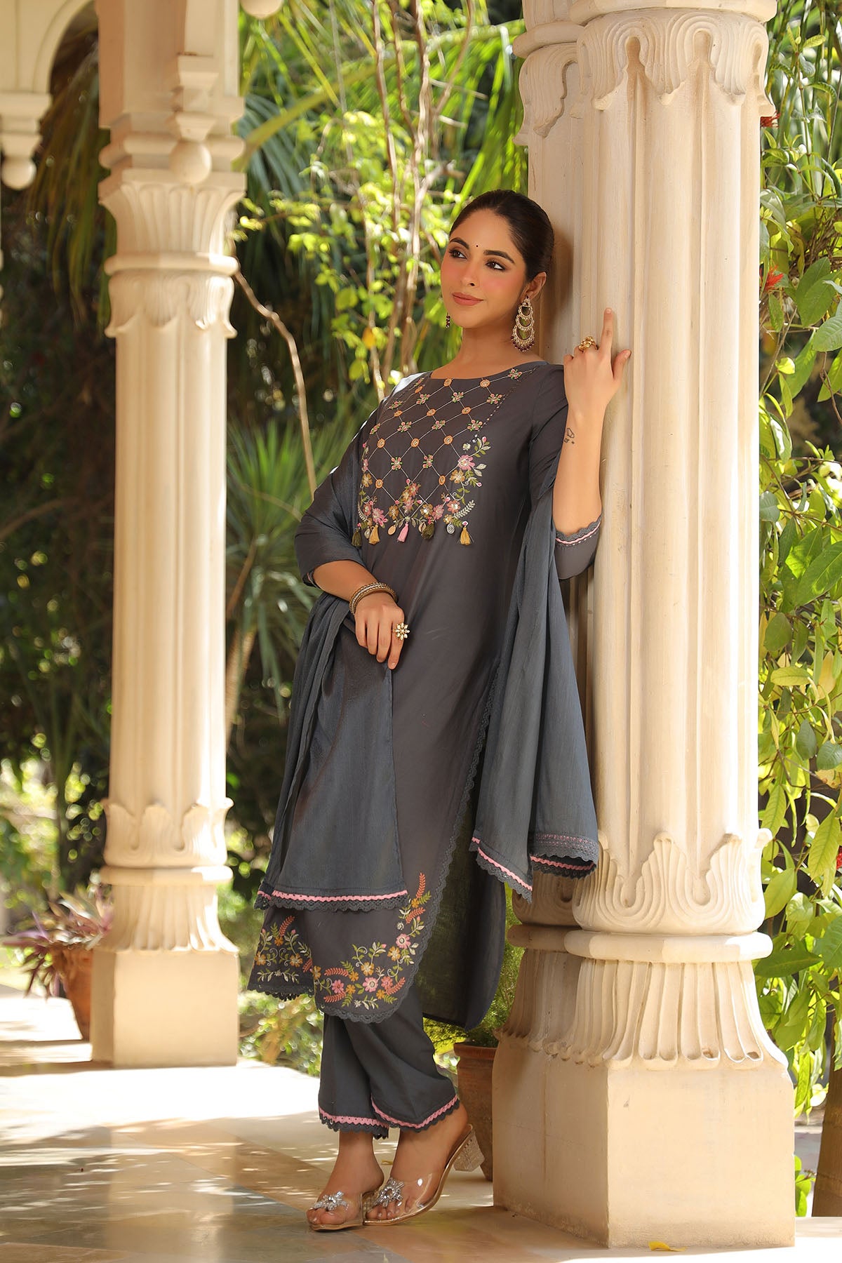 Woman in a dark blue traditional outfit with floral patterns standing against classical architecture.