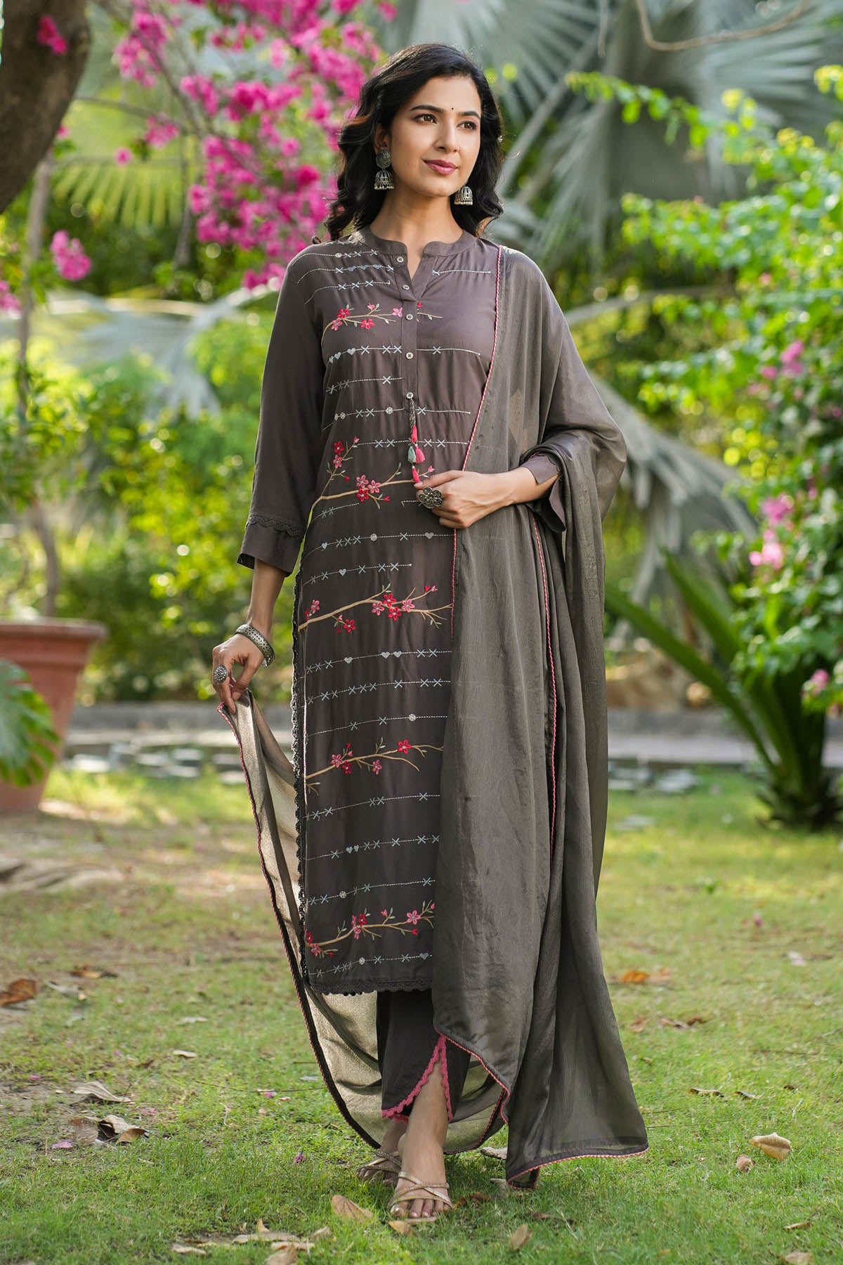 Woman in traditional attire standing in a garden with greenery and flowers.