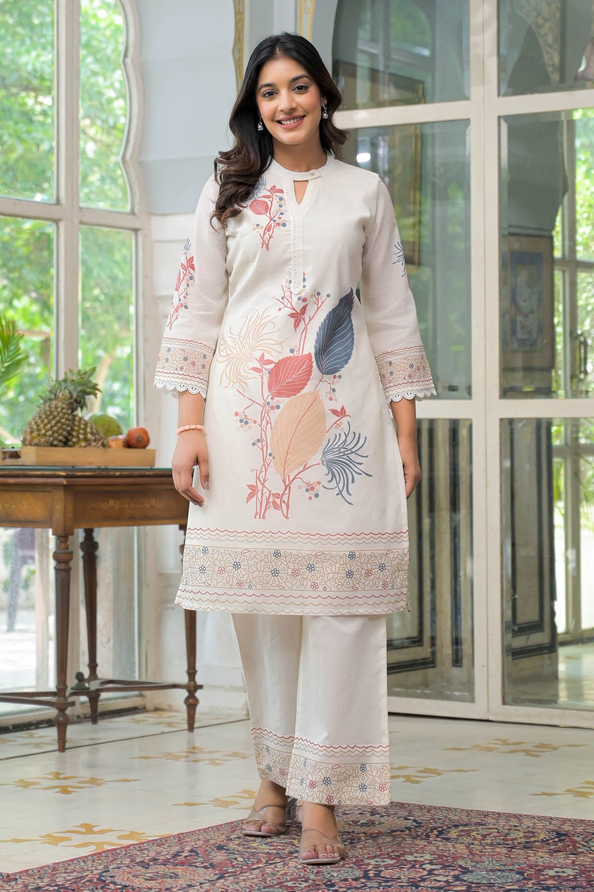 Woman wearing a white embroidered outfit standing in a room with large windows.