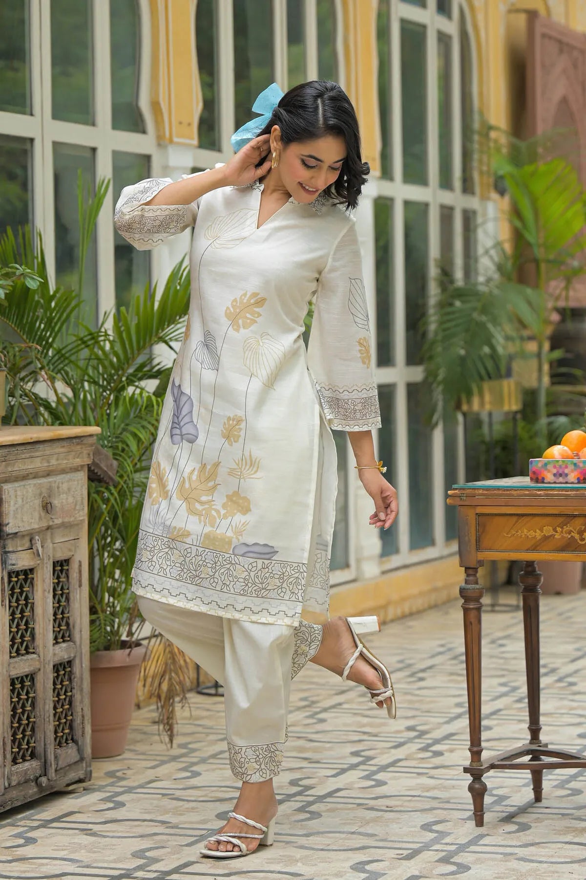 Woman in a white floral kurta with white pants standing in a decorated indoor setting.