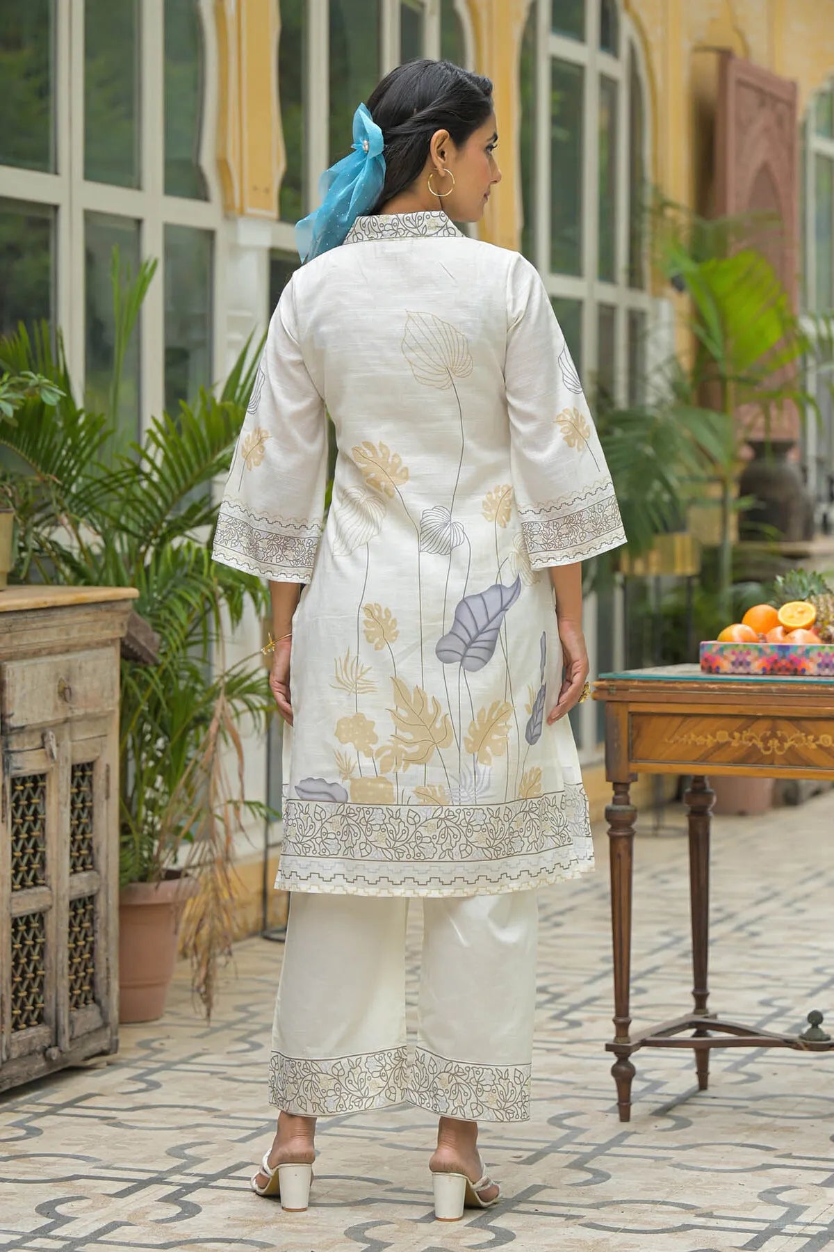 Woman in a white traditional outfit with floral patterns standing in an outdoor setting.