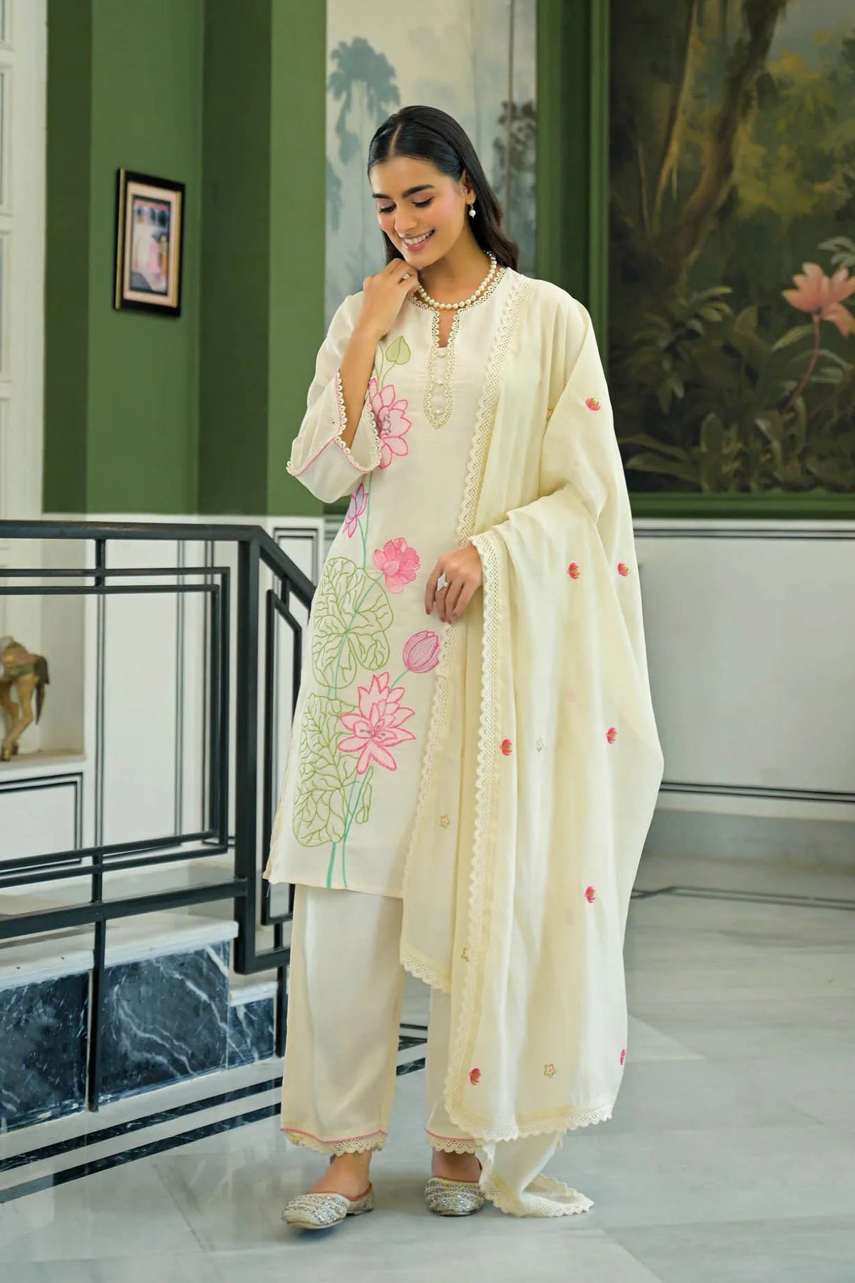 Woman in a cream embroidered outfit standing in a room with decorative elements.
