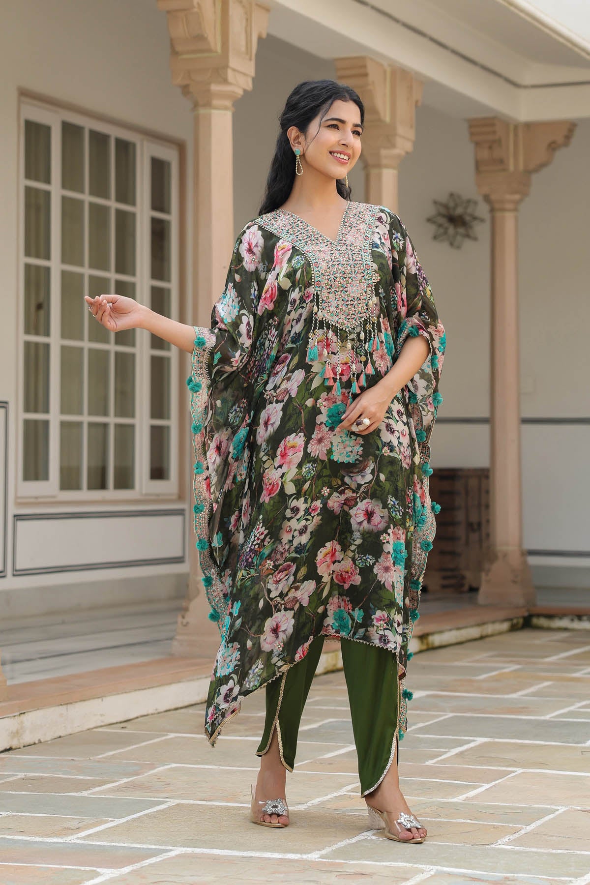 Woman wearing a floral dress and green pants standing in front of a building.
