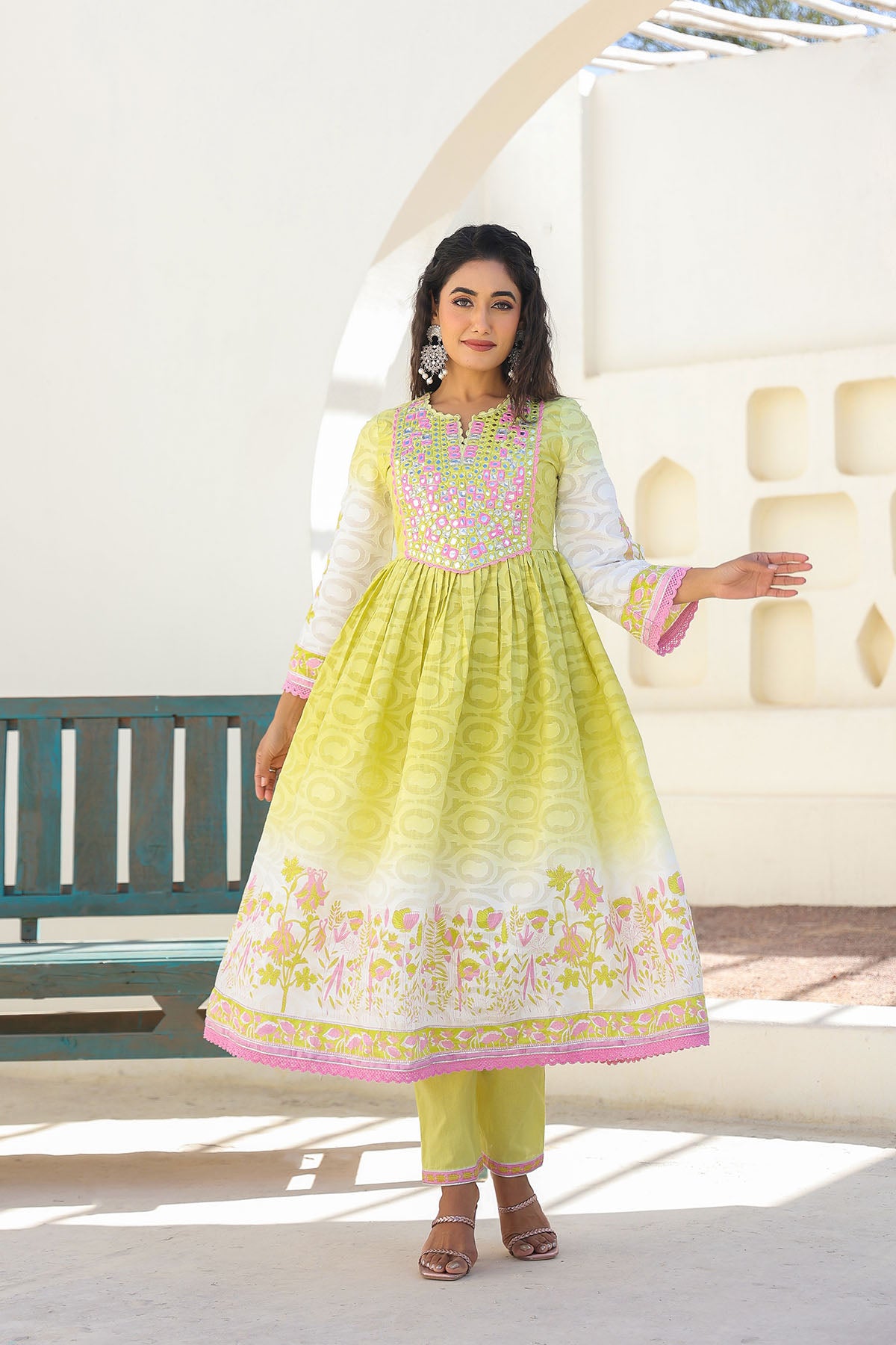 Woman wearing a light green traditional outfit with white and pink details, standing indoors.