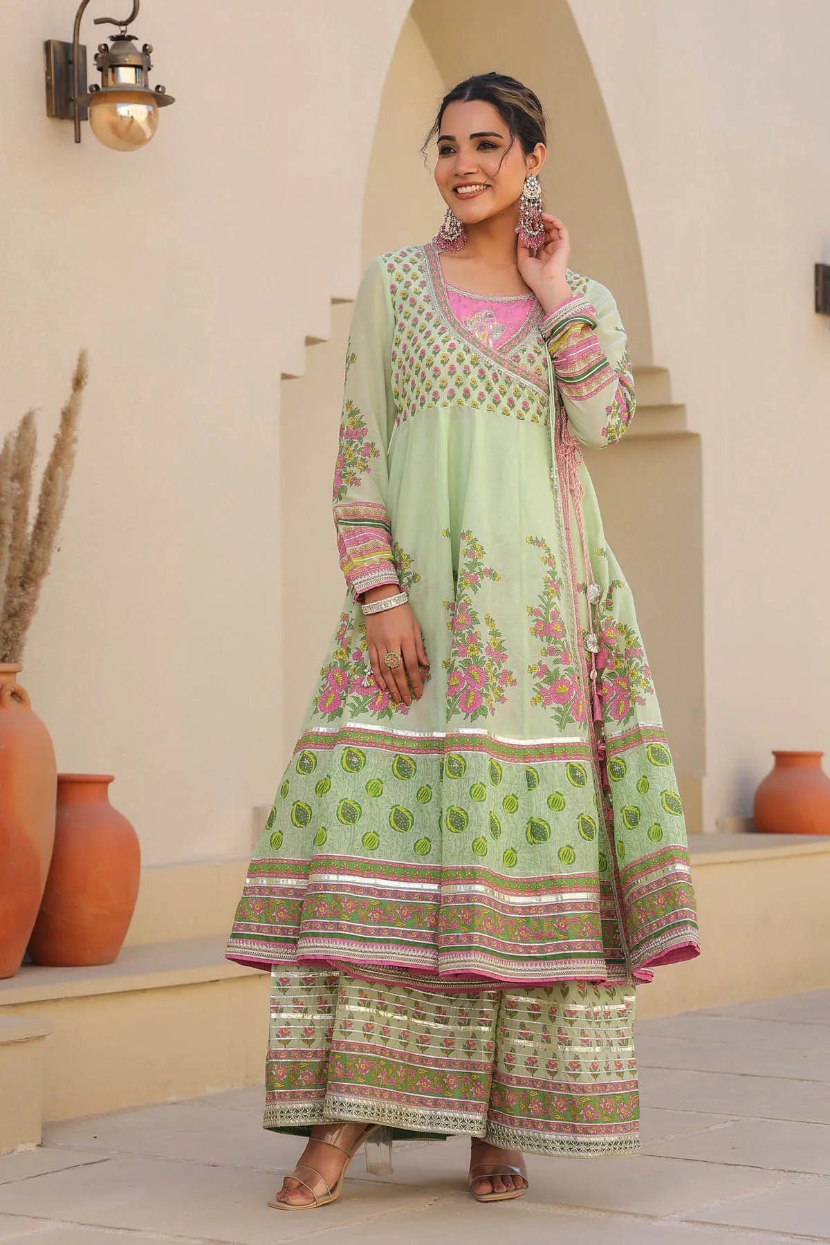 Woman in a light green traditional outfit with pink accents standing in an outdoor setting.