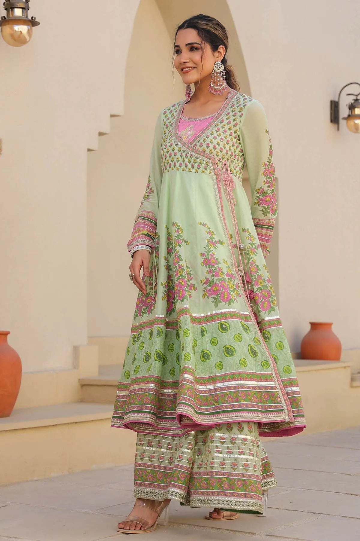 Woman wearing a light green traditional outfit with pink and white patterns in an indoor setting.
