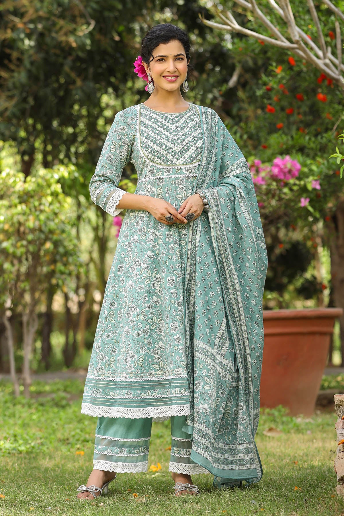 Woman in a light blue traditional outfit standing outdoors with greenery in the background