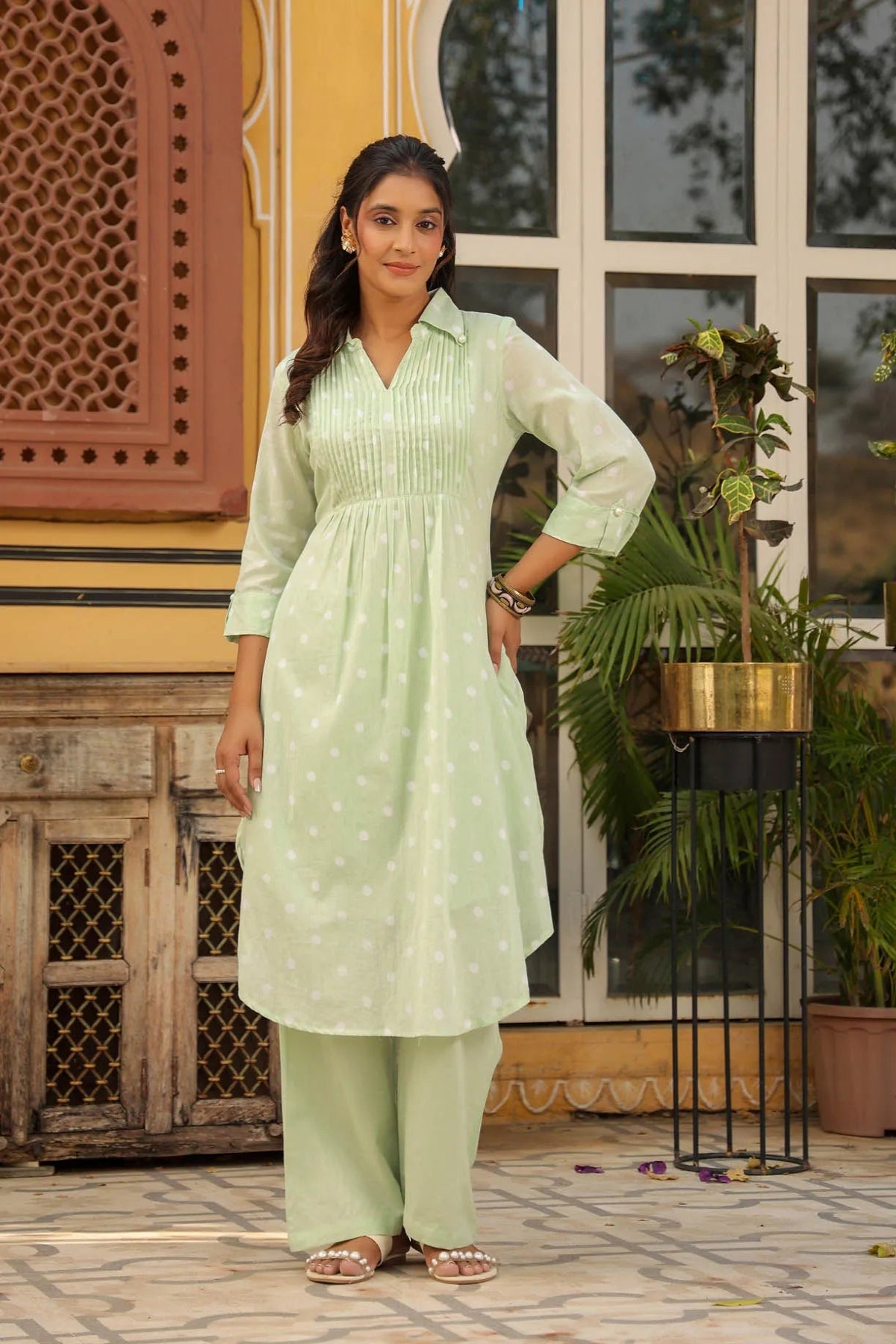 Woman in a light green traditional outfit standing in front of a decorative building entrance.