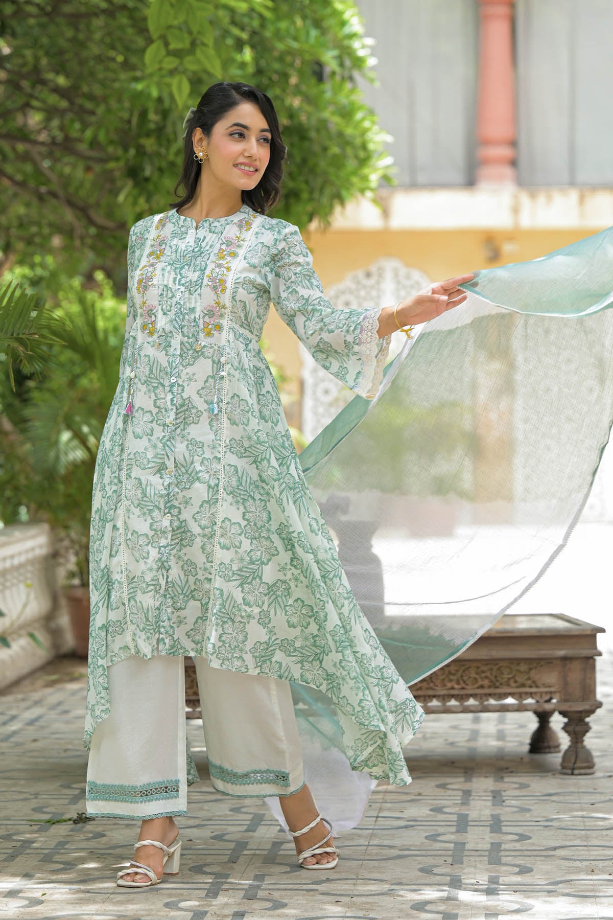 Woman in a light green and white traditional outfit with a matching dupatta, standing outdoors.
