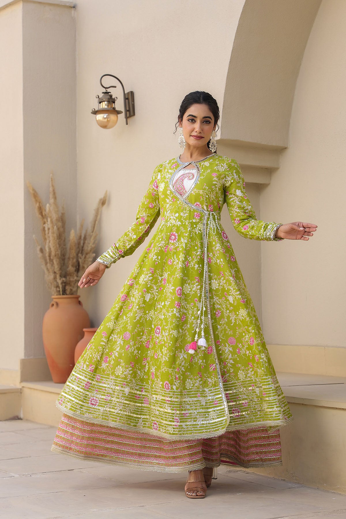 Woman in a green floral dress standing in a well-lit room with decorative elements.
